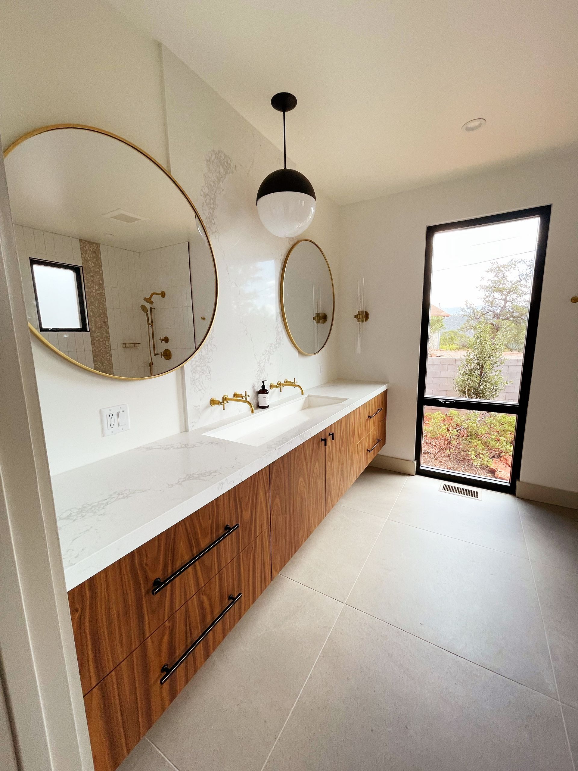 A bathroom with two sinks , two mirrors and a window.