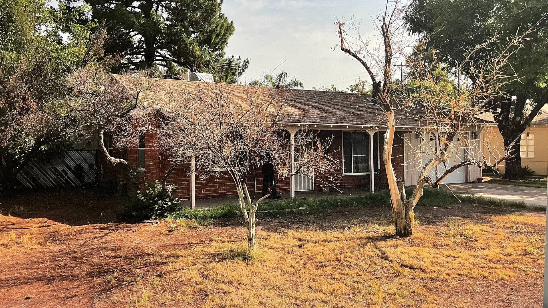 A brick house with a porch and trees in front of it.