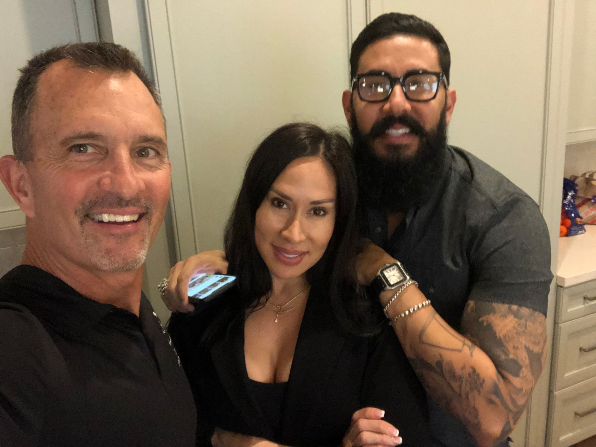 Two men and a woman are posing for a picture in a kitchen.