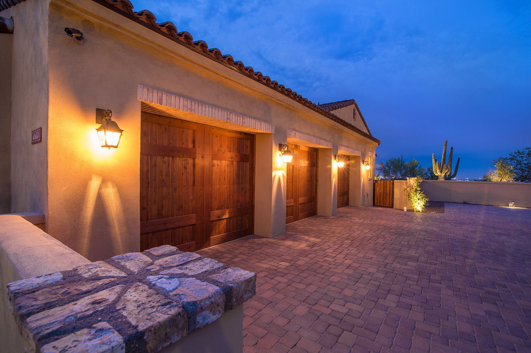 A large house with three garage doors and a brick driveway at night.