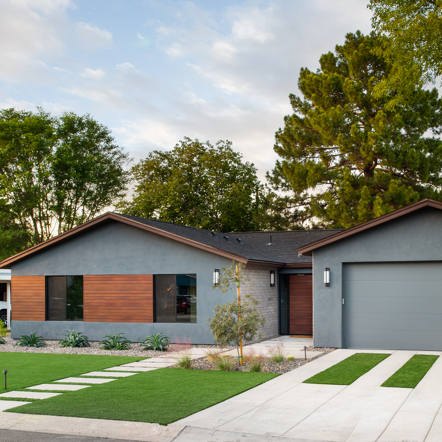 A gray house with a driveway and trees in the background