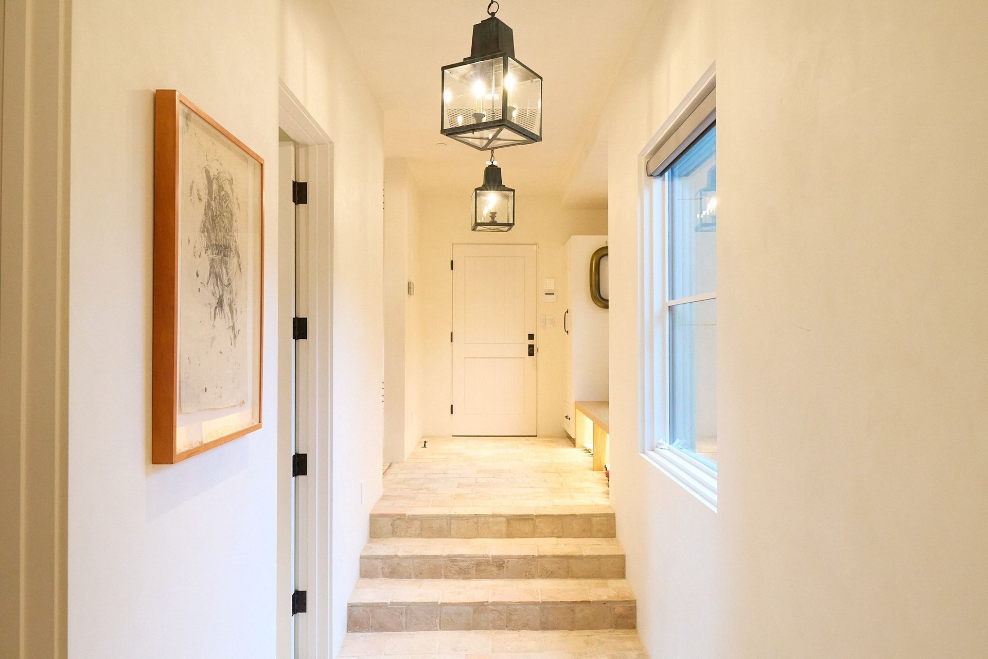 A hallway with stairs leading up to a door and two lanterns hanging from the ceiling.