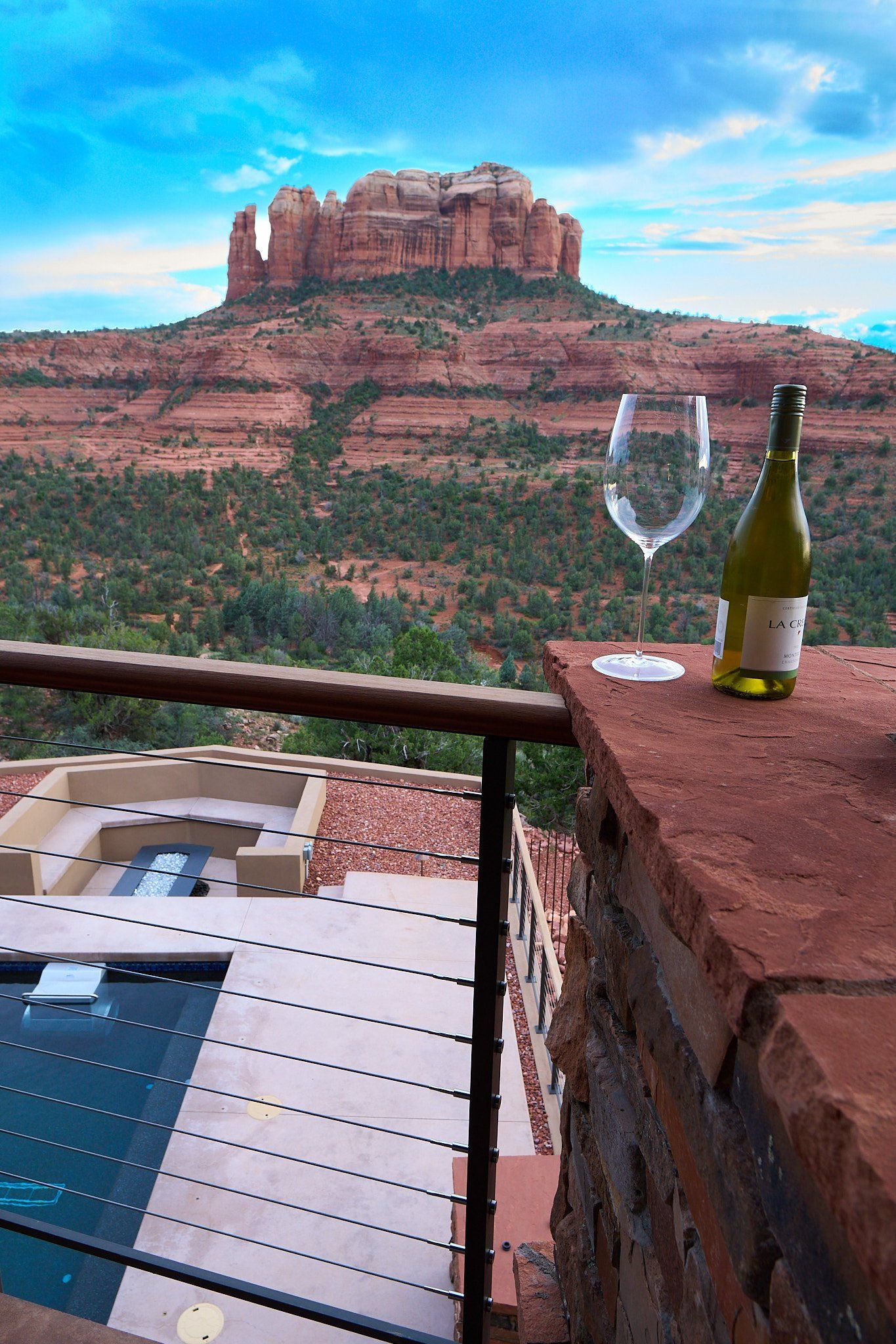 A bottle of wine and a glass of wine are on a balcony overlooking a mountain.