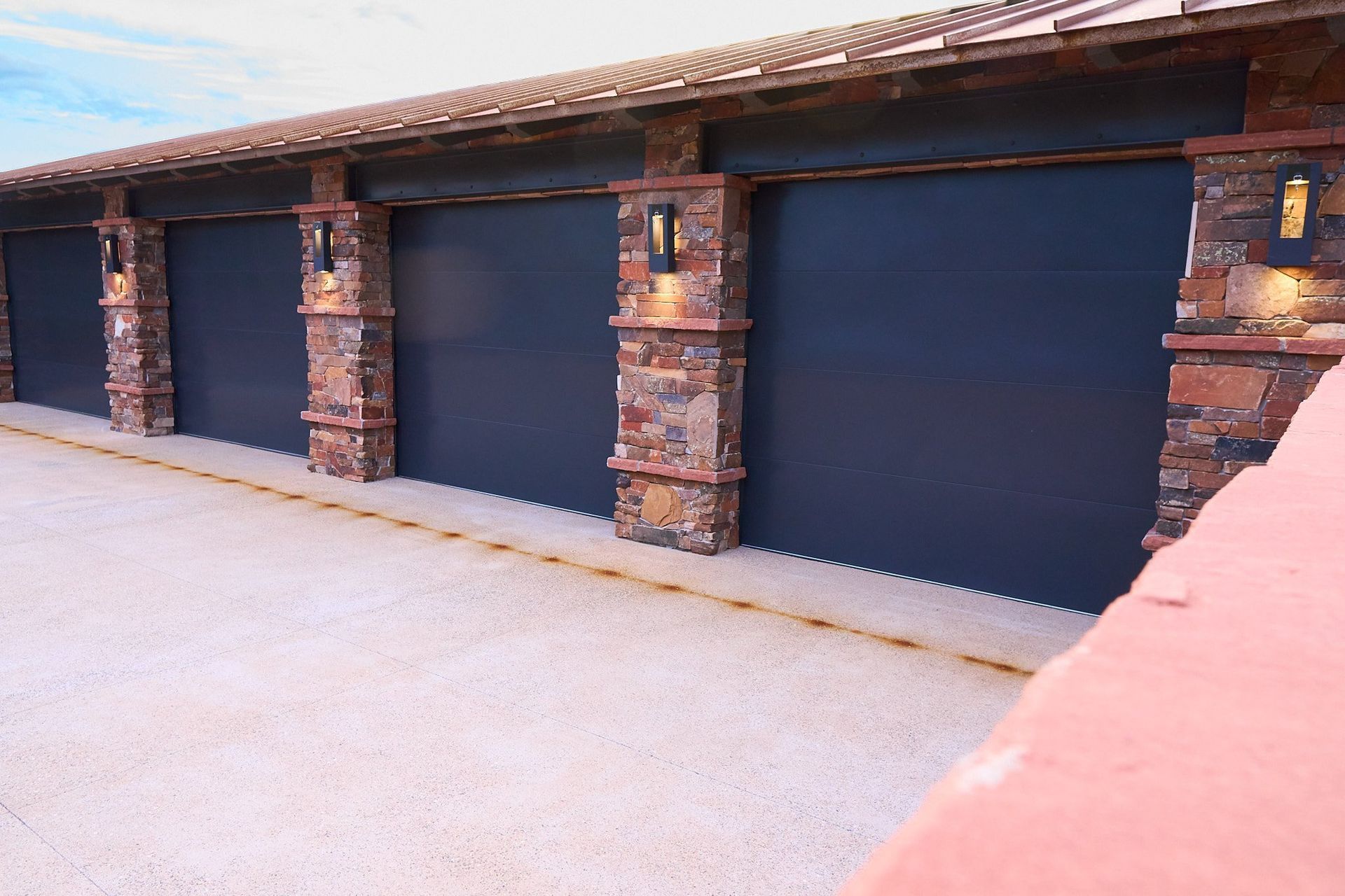 A row of black garage doors with brick pillars