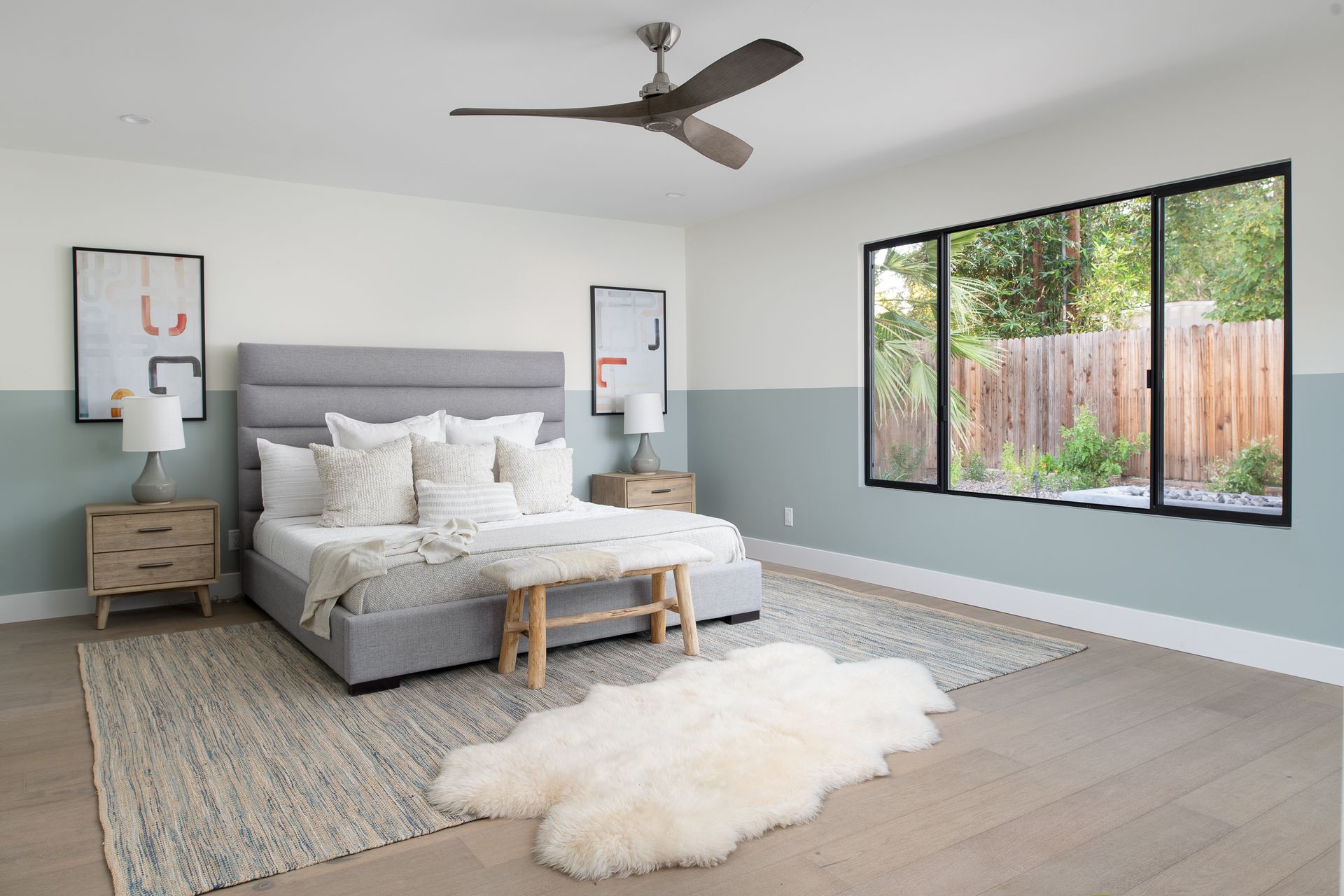 A bedroom with a bed , a rug , a ceiling fan , and two windows.