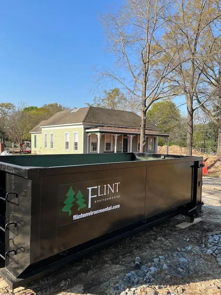 Black dumpster in front of a house under construction, Flint Disposal logo on side.