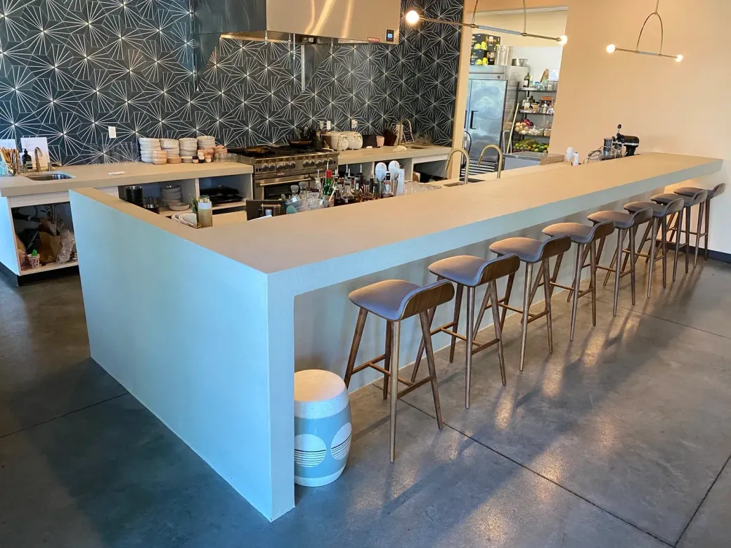 Modern kitchen with a long white bar, stools, and cooking area.