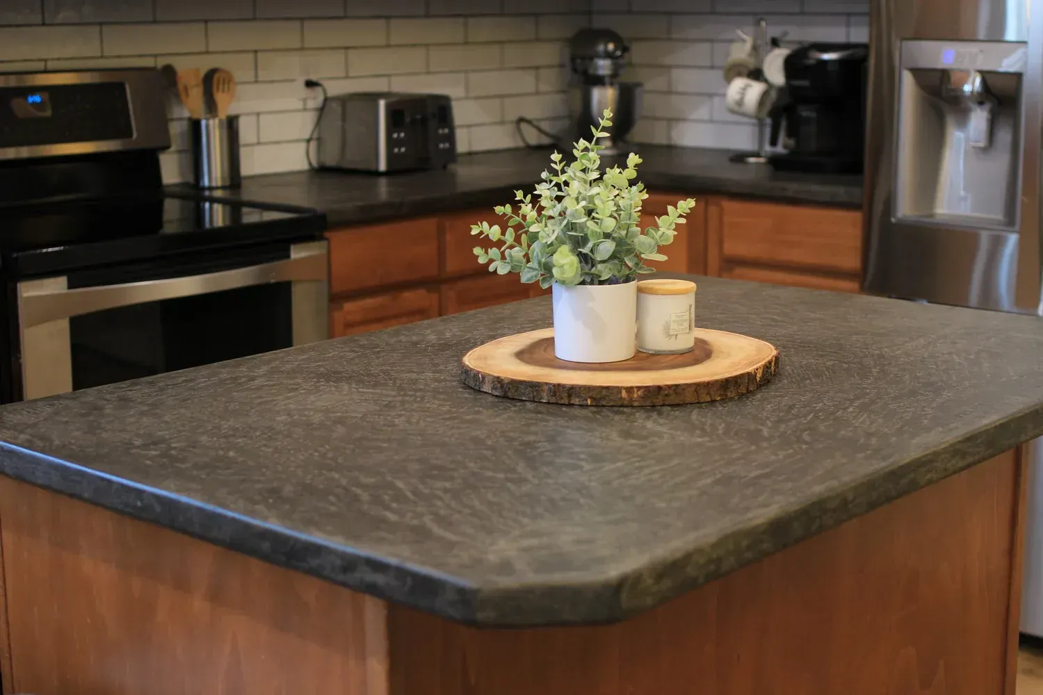Kitchen island with dark countertop, wood base, and plant centerpiece. Background: stove, cabinets, and appliances.