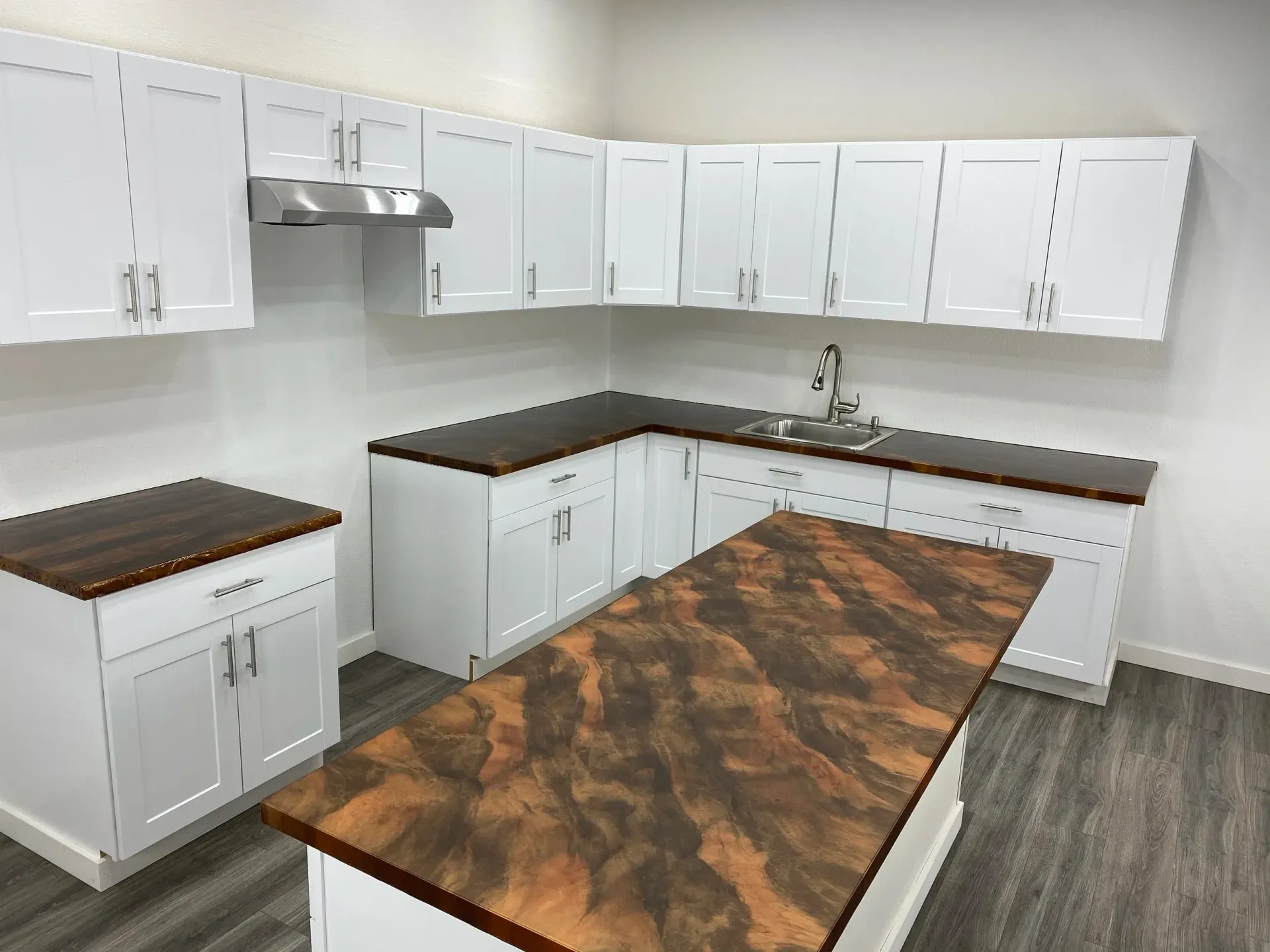 White kitchen cabinets with dark countertops and an island, stainless steel range hood, and sink.