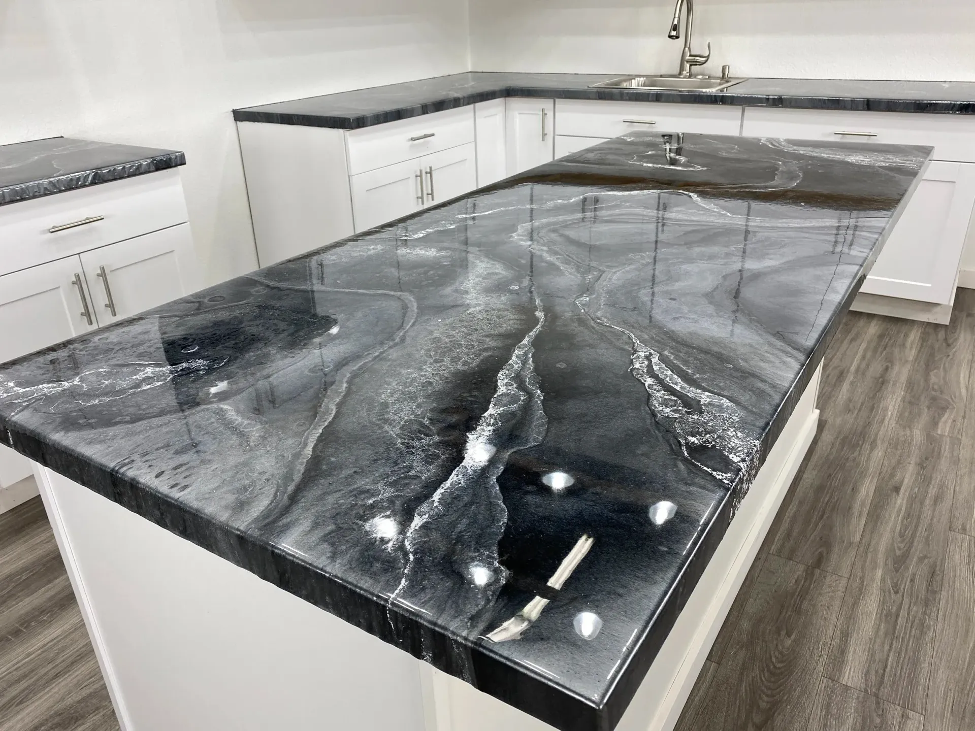 Black and white epoxy kitchen countertop with silver waves, white cabinets, and light gray flooring.