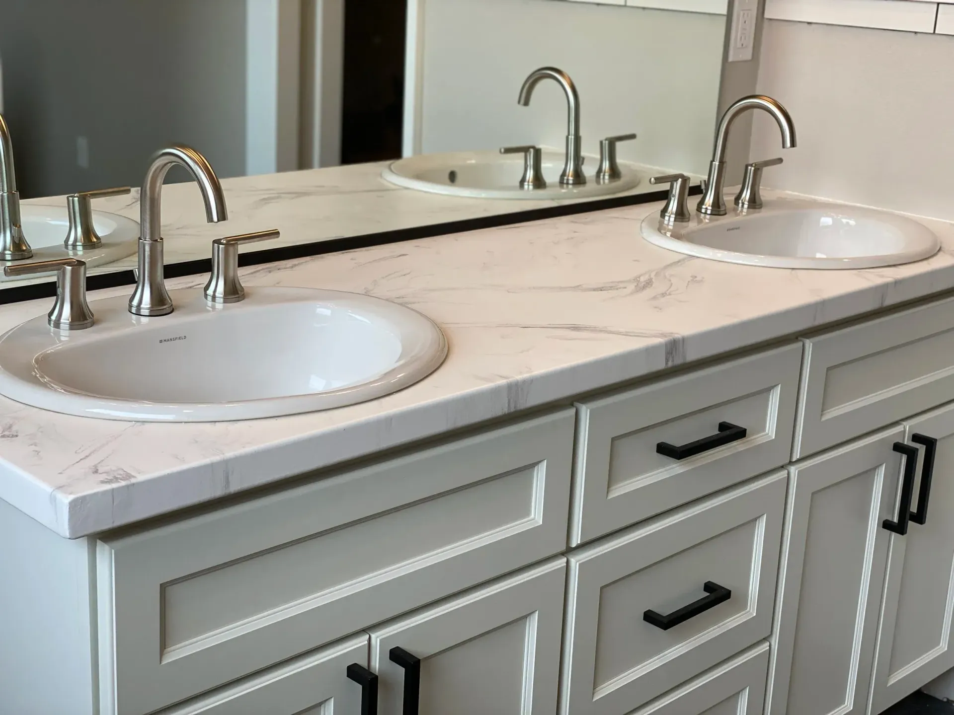 Bathroom vanity with two sinks, white countertop, and gray cabinets with black handles.
