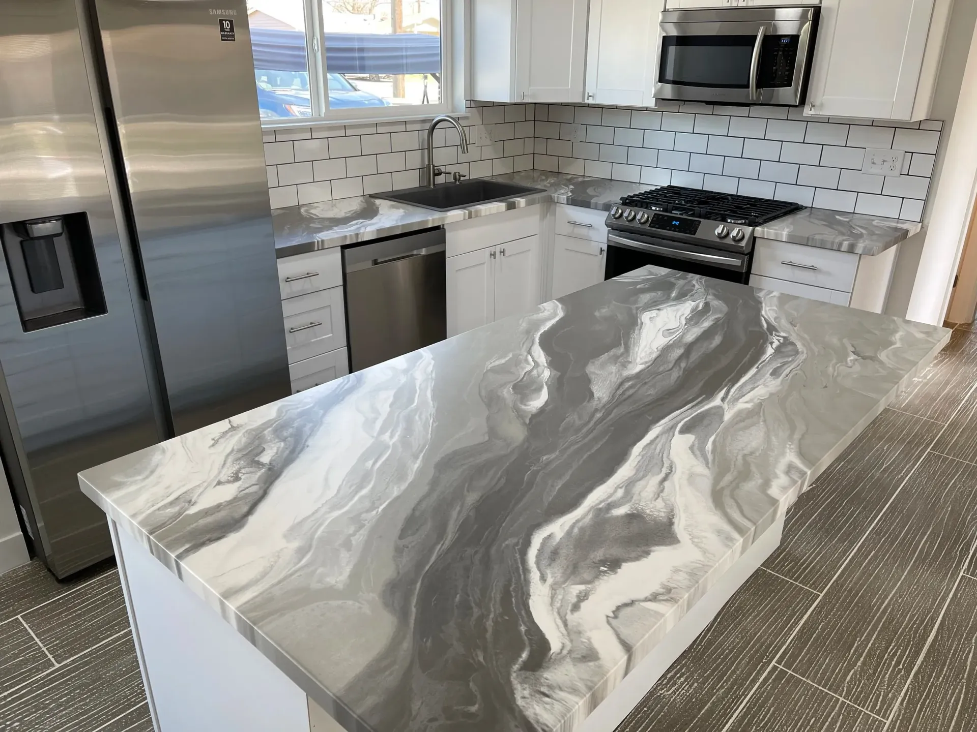 Modern kitchen with gray and white countertop, stainless steel appliances, and white cabinets.