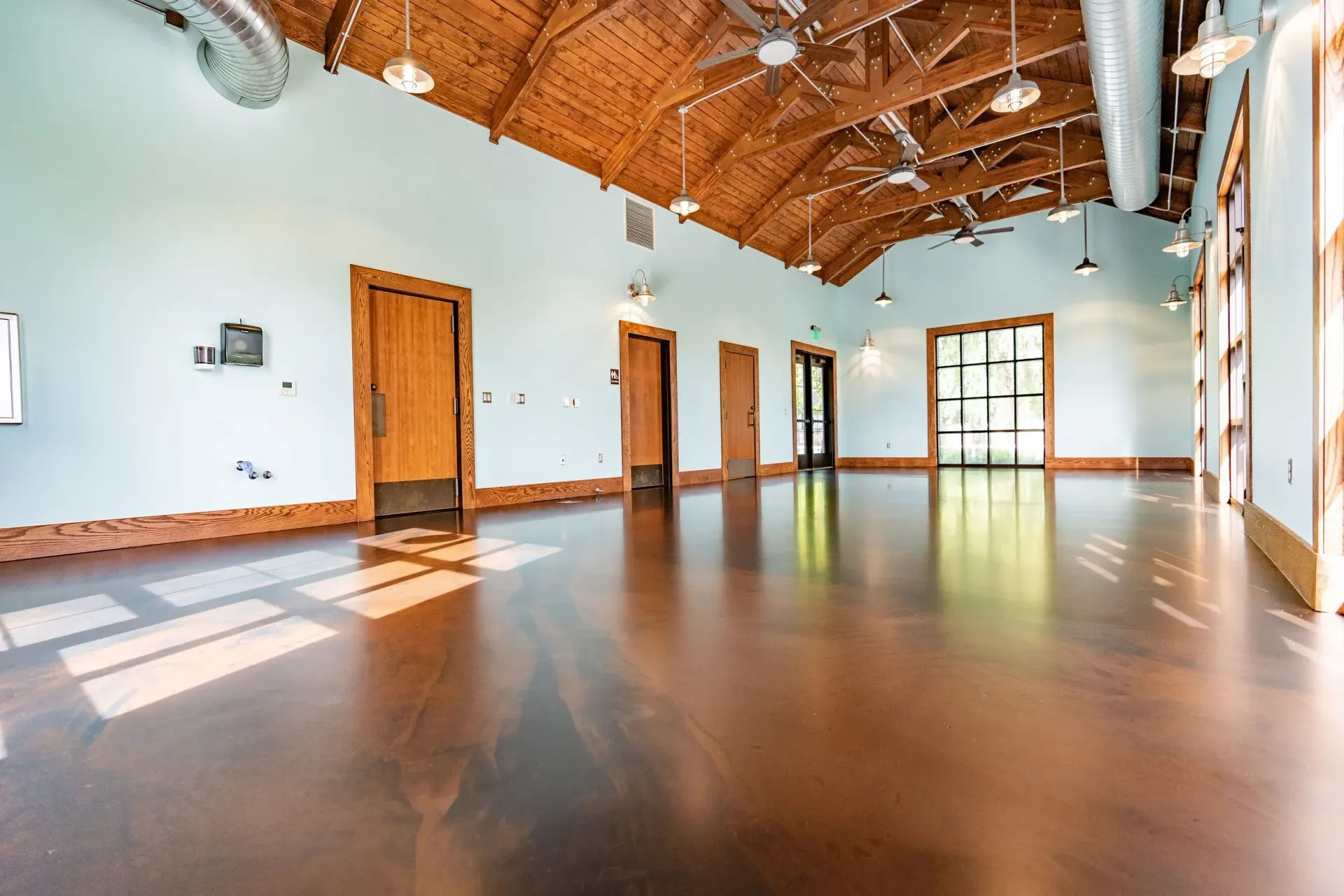 Large, bright room with wood floors, pale blue walls, and a vaulted wood ceiling. Sunlight streams through windows.