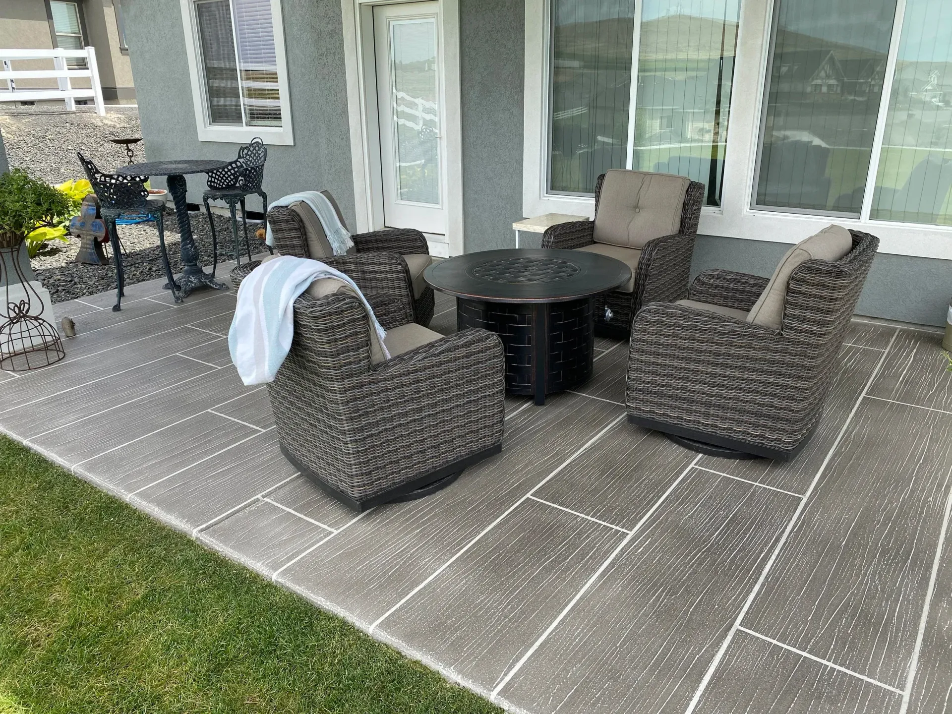 Patio with four wicker chairs and a fire pit table. White towel on one chair.