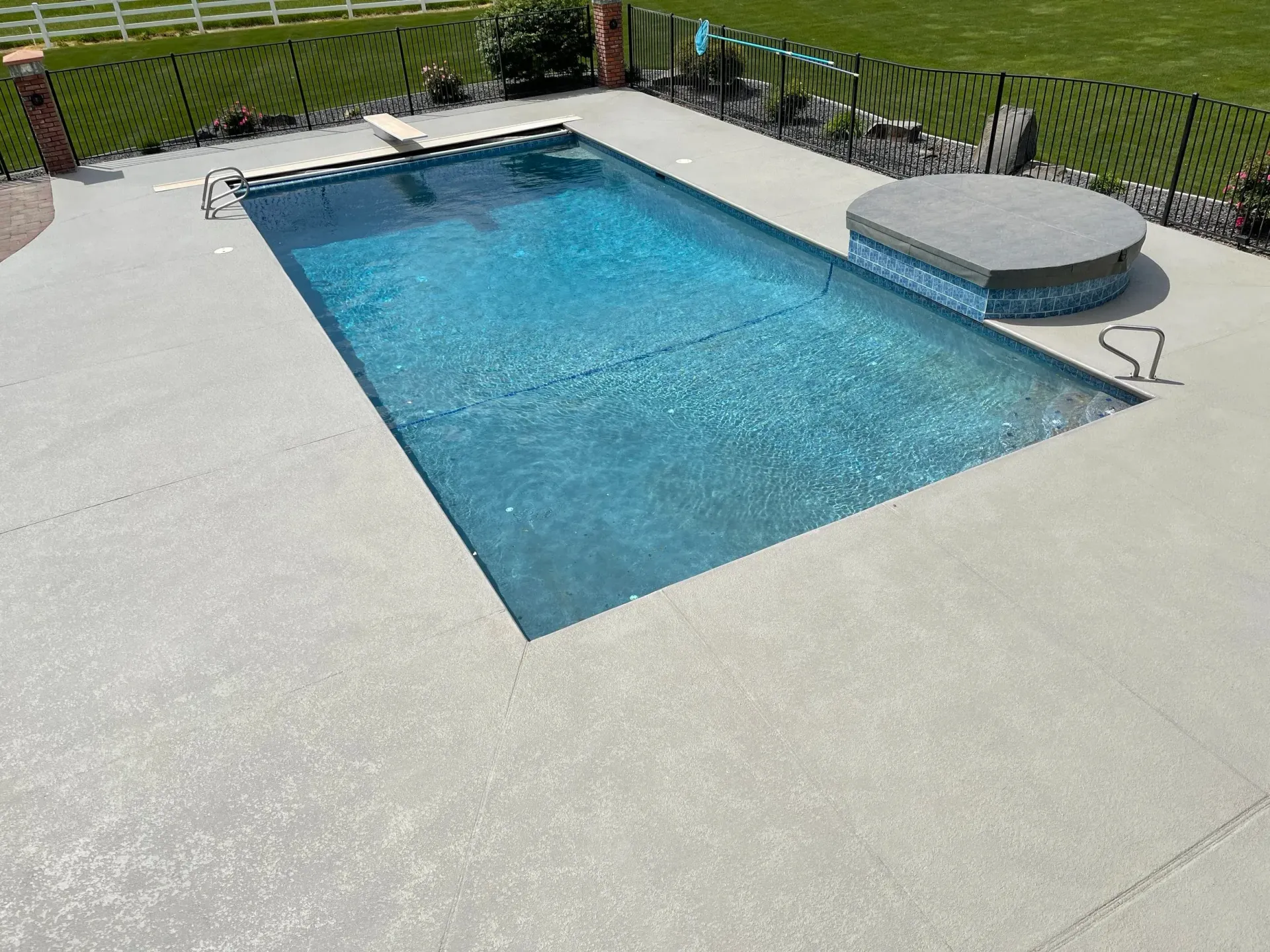 Rectangular swimming pool surrounded by light gray concrete; a covered hot tub sits nearby.