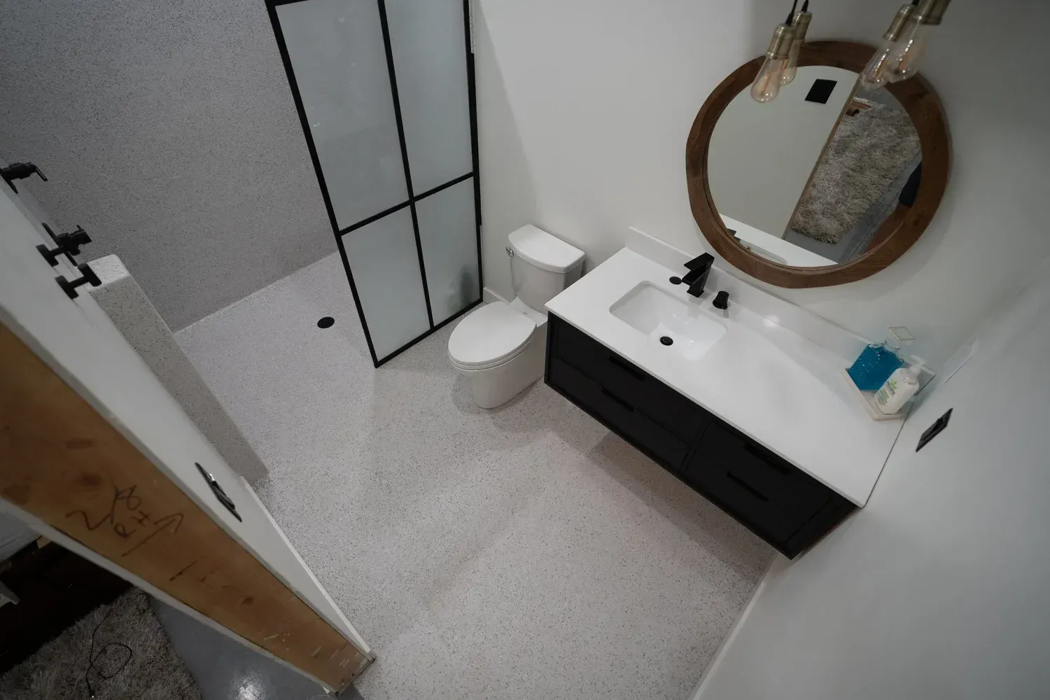 Modern bathroom with black vanity, white countertop, round mirror, and speckled floor.