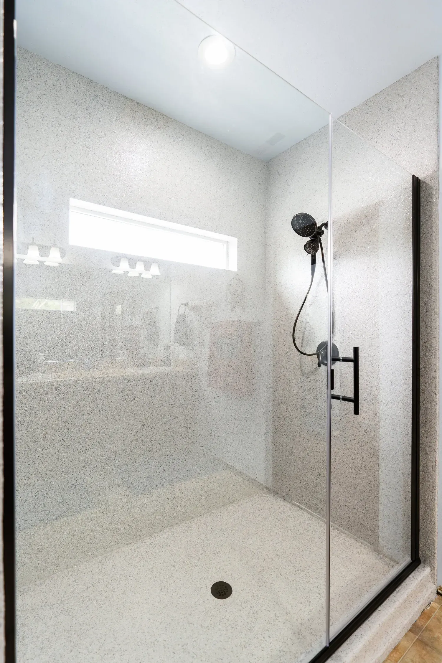 Shower with black frame, pebbled walls and floor, glass door, and black showerhead.