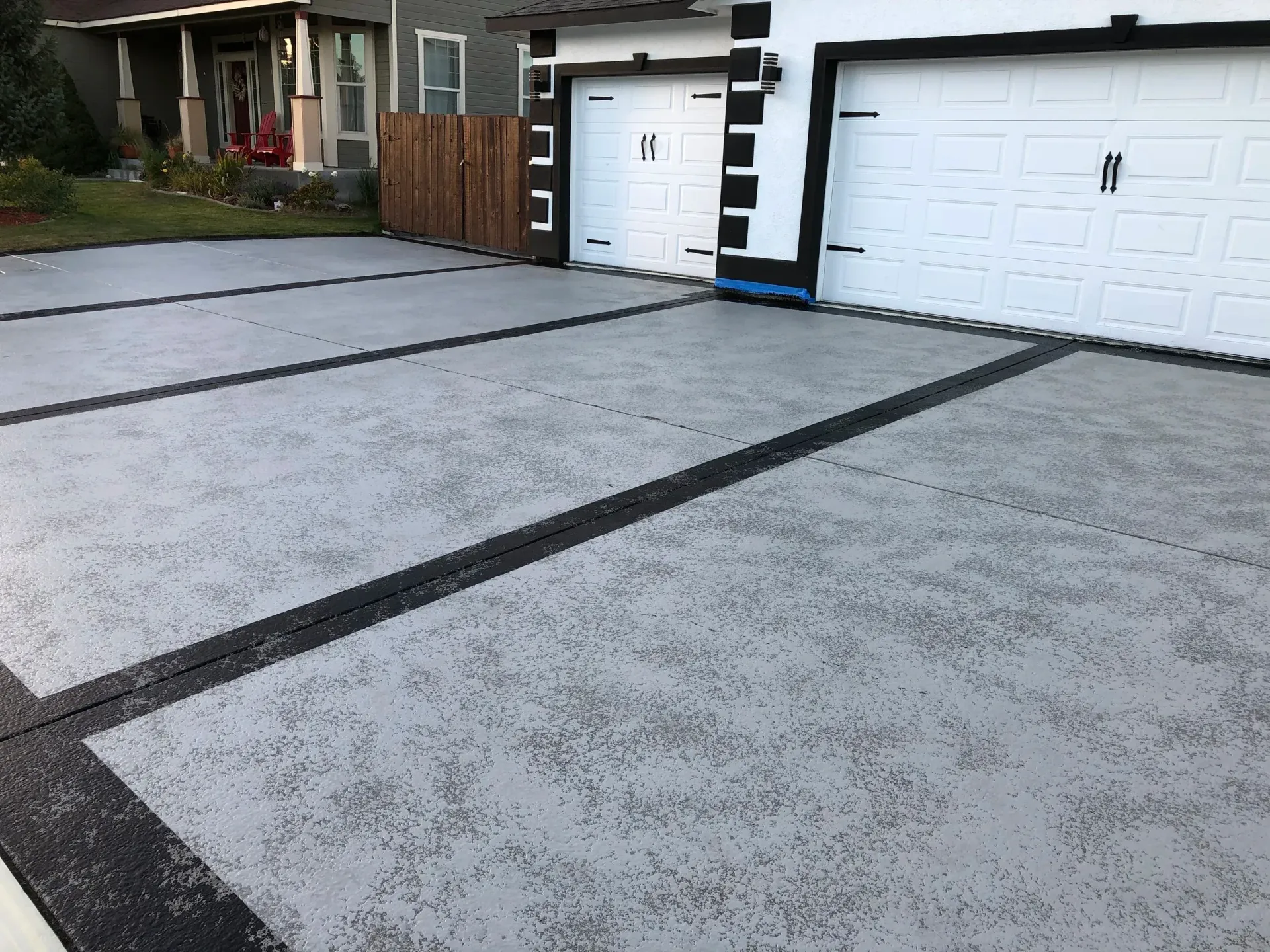 Gray concrete driveway with black lines and white garage doors.