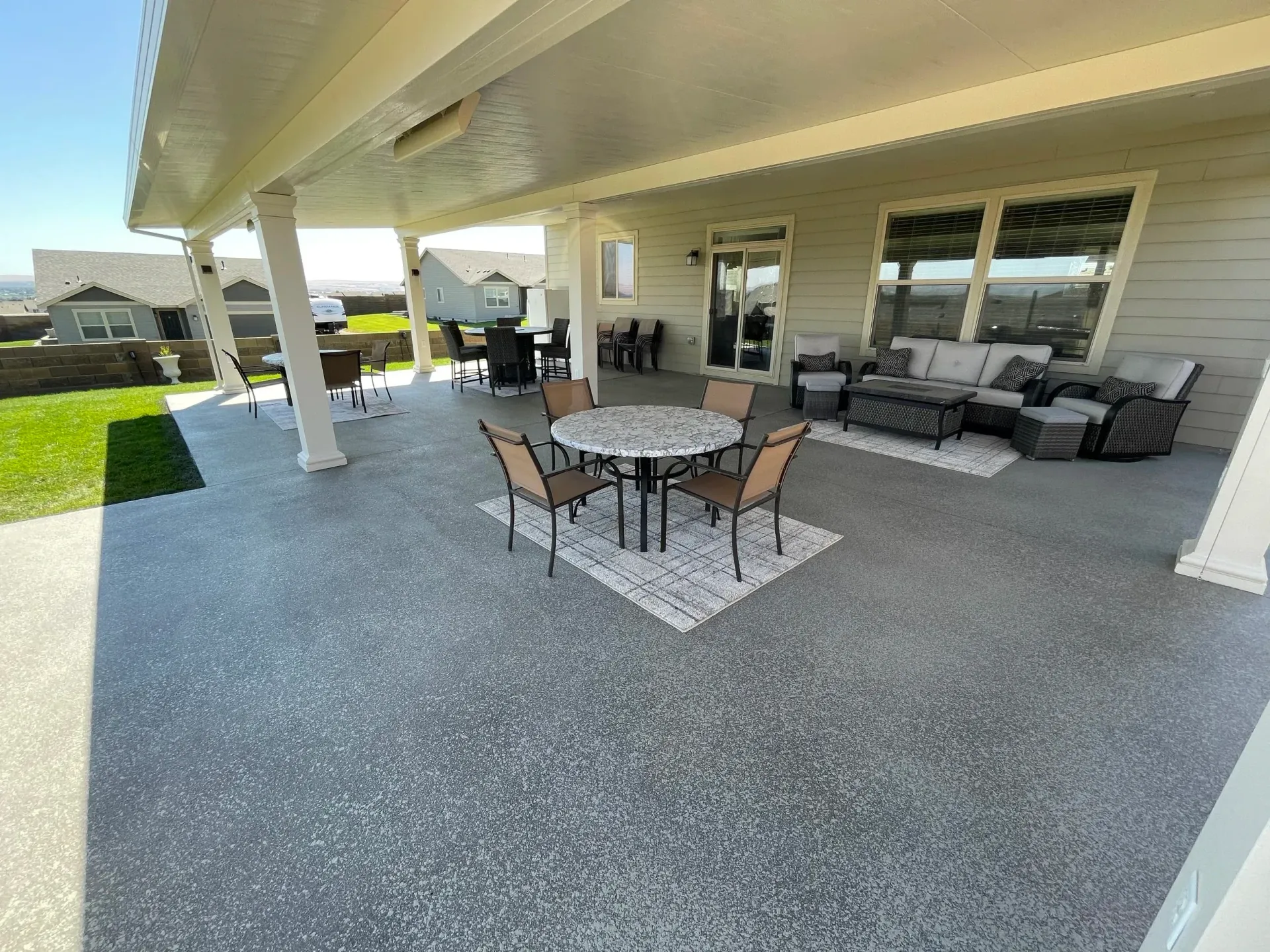 Covered patio with outdoor furniture, grey concrete floor, and a view of a grassy yard.