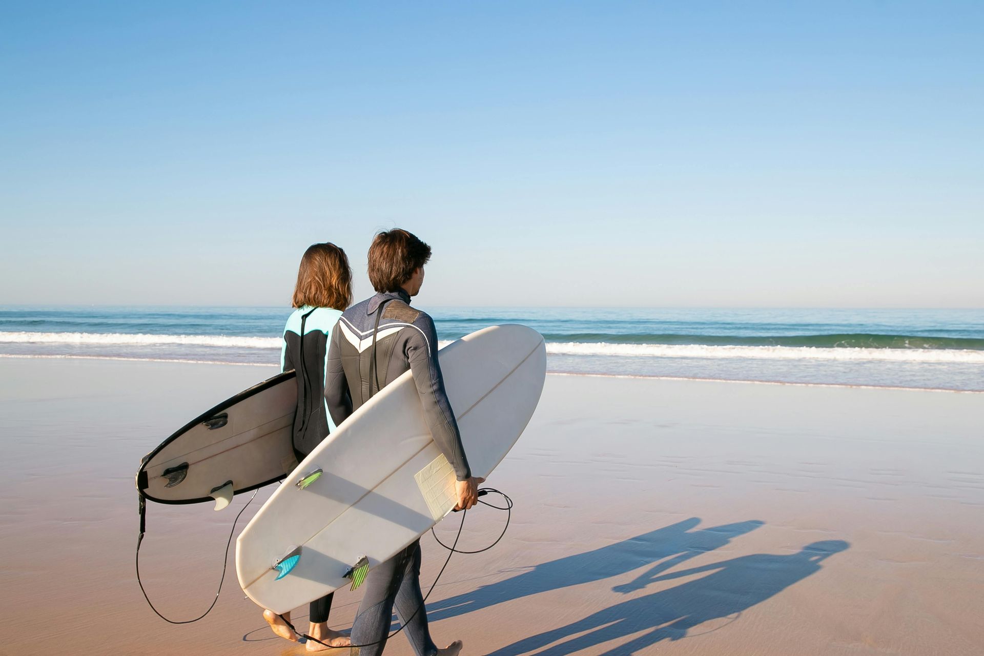 Two people walking the beach with surfboards