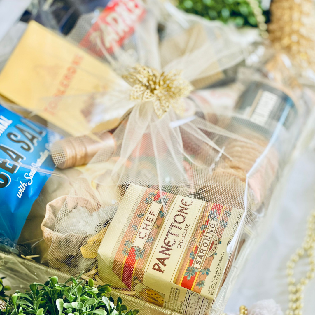 A festive gourmet hamper wrapped in gold mesh, featuring artisan panettone, sea salt crisps, and assorted premium snacks, finished with a decorative gold flower.