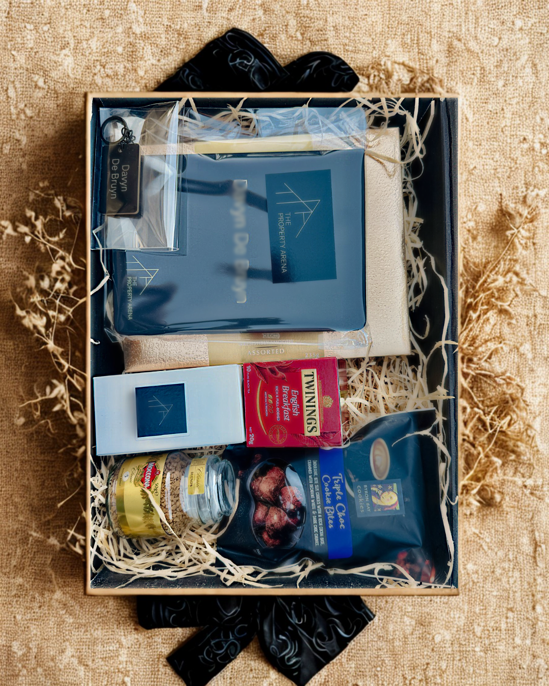 Branded corporate gift box featuring premium items like Twinings tea and The Property Arena merchandise, styled with natural textures and personal touches.