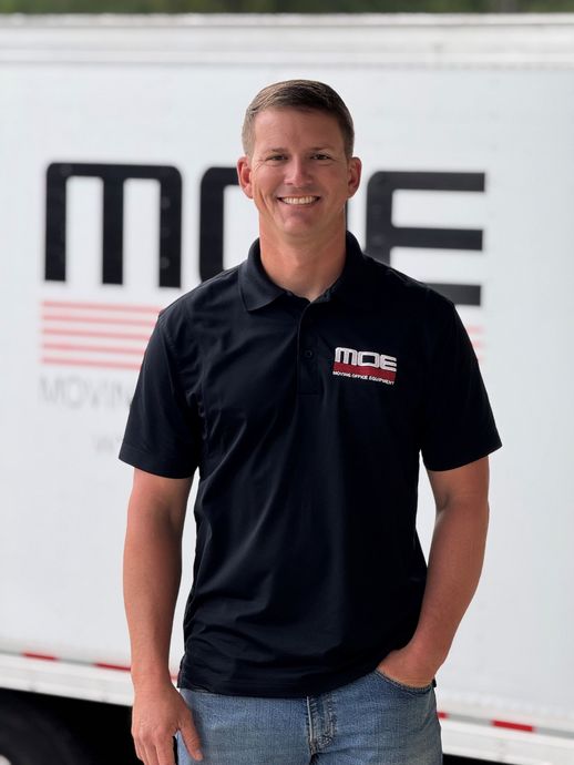 Man standing in front of a white trailer, wearing a black polo shirt with a company logo.