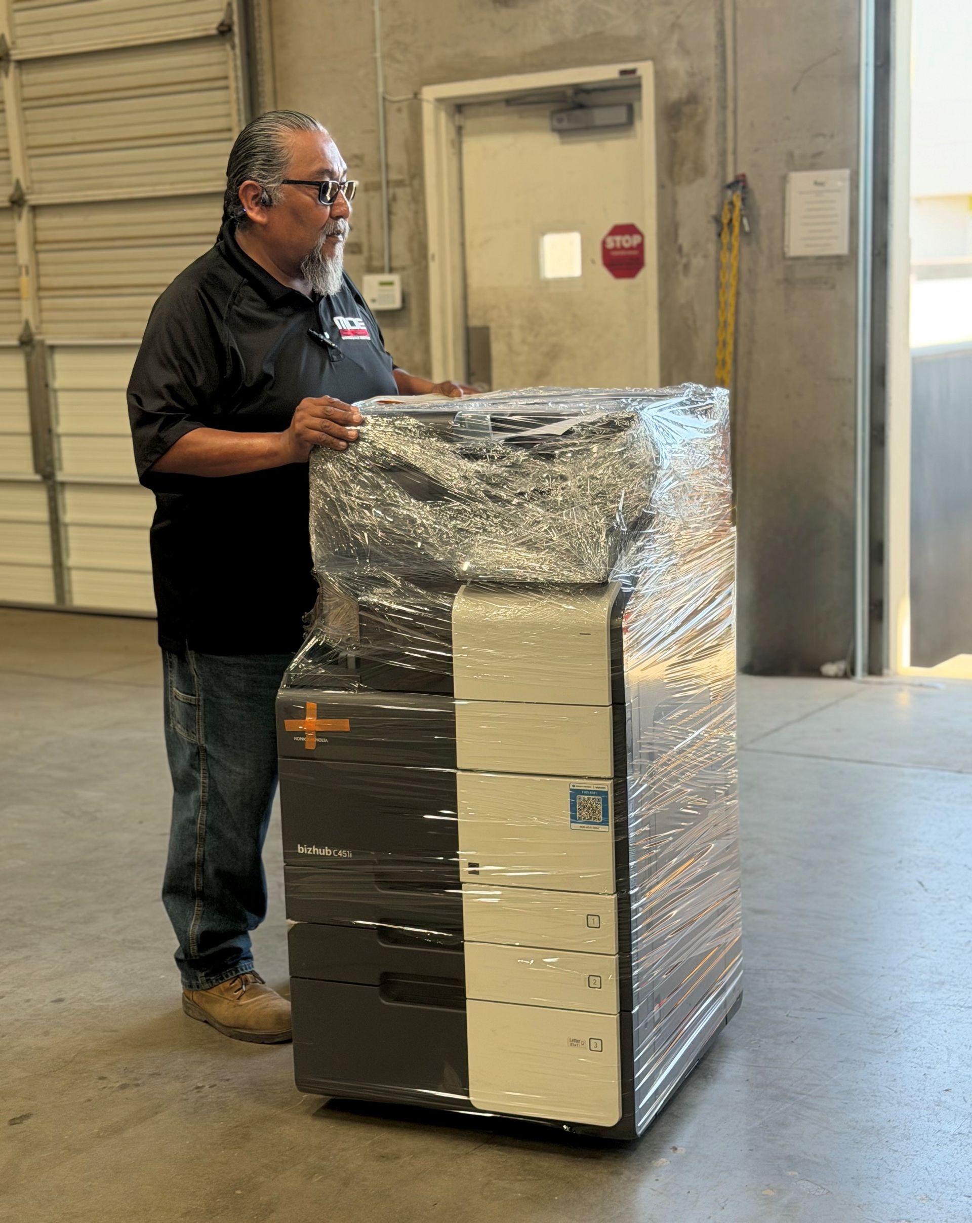Man standing beside a foil-wrapped appliance in a warehouse doorway