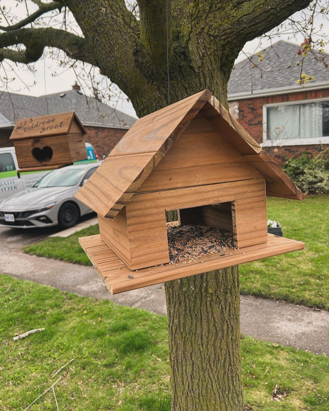 A wooden birdhouse is hanging from a tree in a yard.