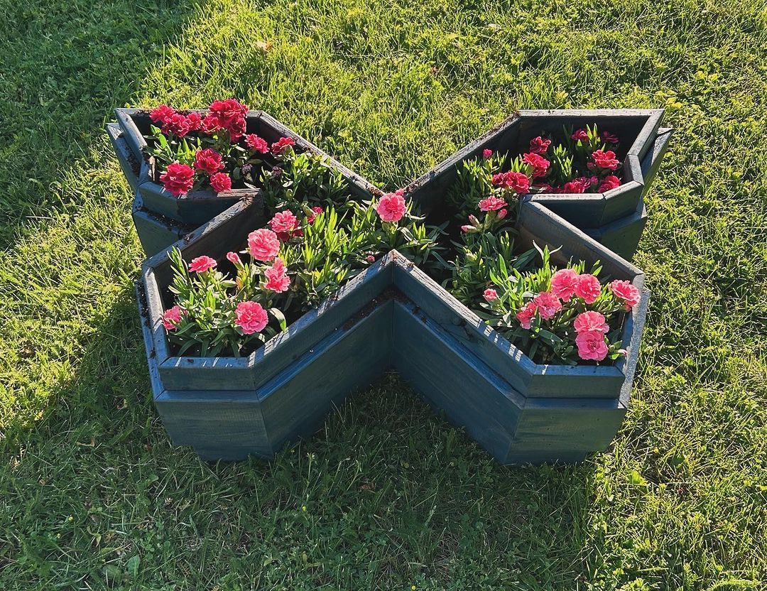 A butterfly shaped planter filled with pink flowers is sitting in the grass.