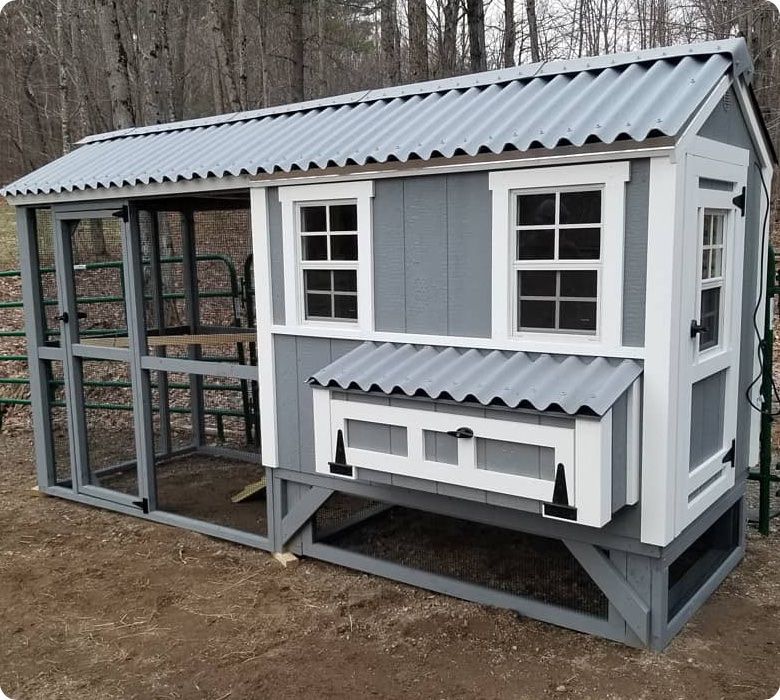 A chicken coop with a white door and windows is sitting in the dirt.