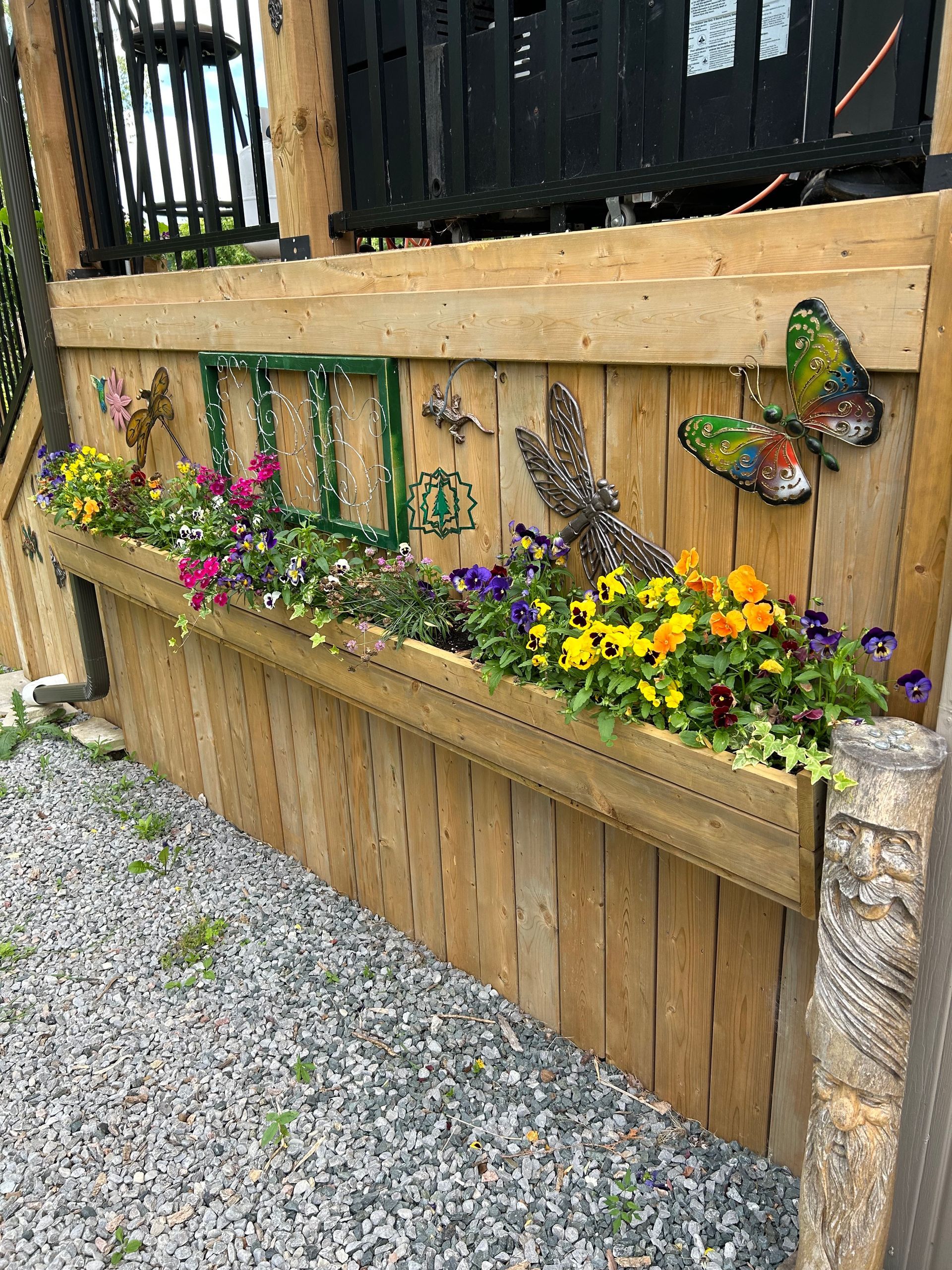 A wooden fence with a planter filled with flowers and butterflies on it.