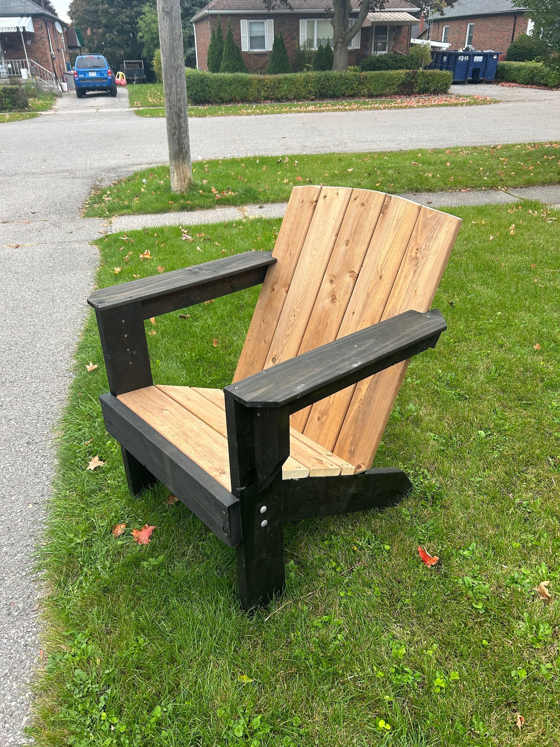 A wooden chair is sitting in the grass on the side of the road.
