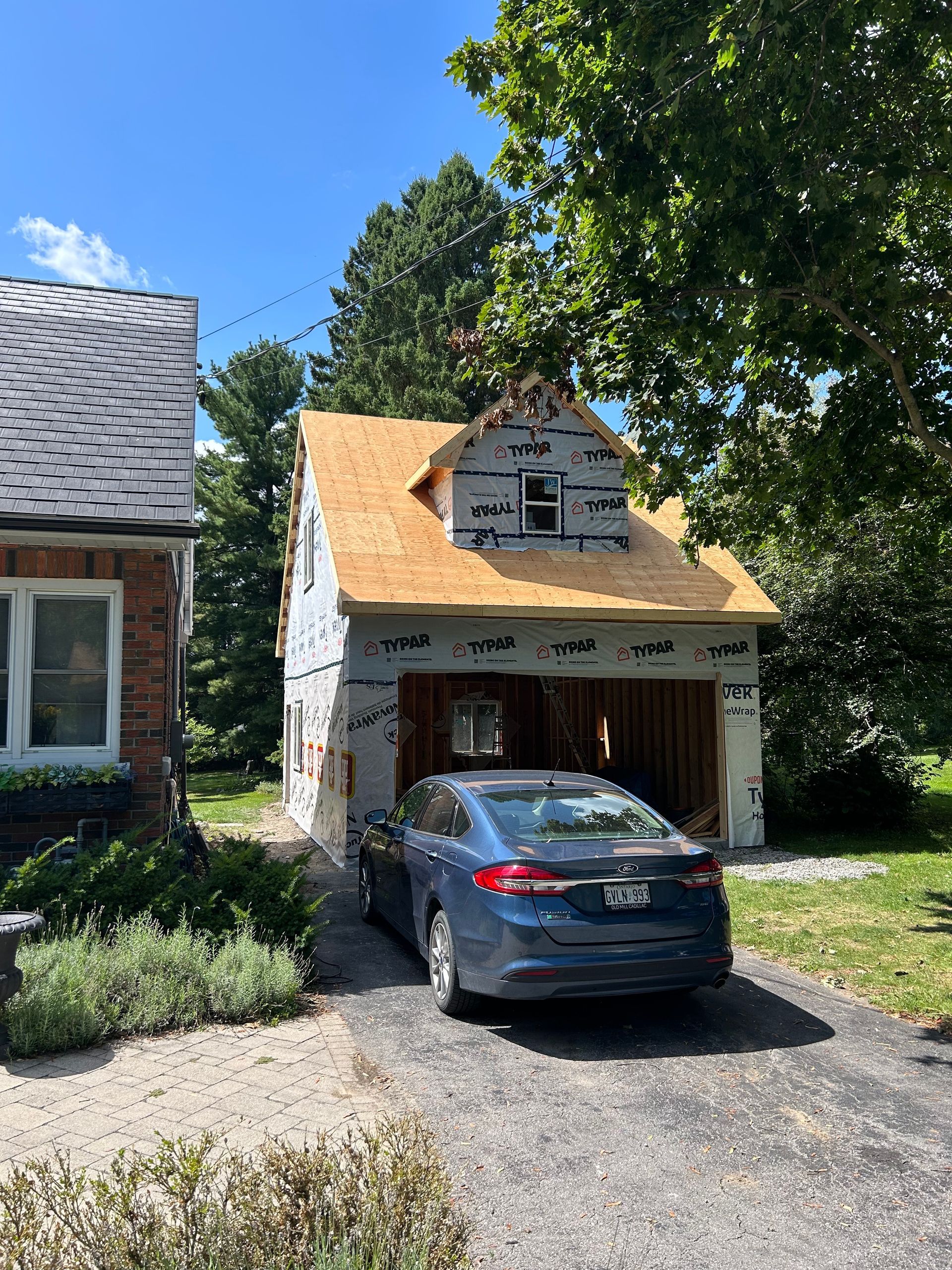 A car is parked in front of a garage that is being remodeled.