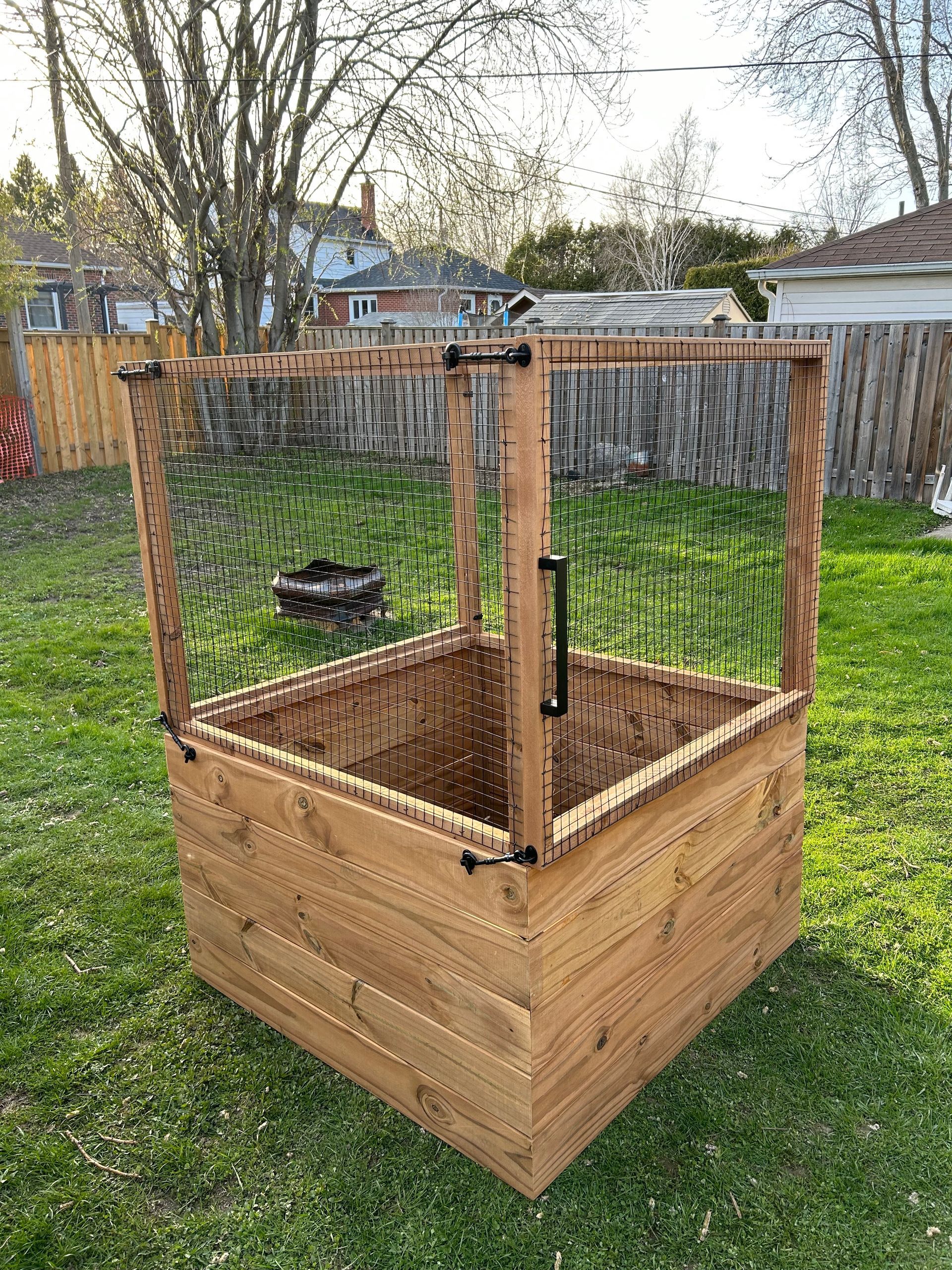 A wooden box with a fence around it is sitting in the grass in a backyard.