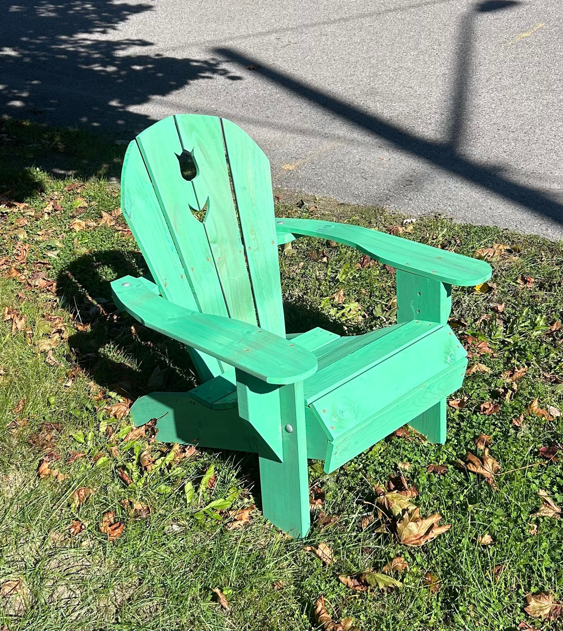 A green wooden adirondack chair is sitting in the grass.