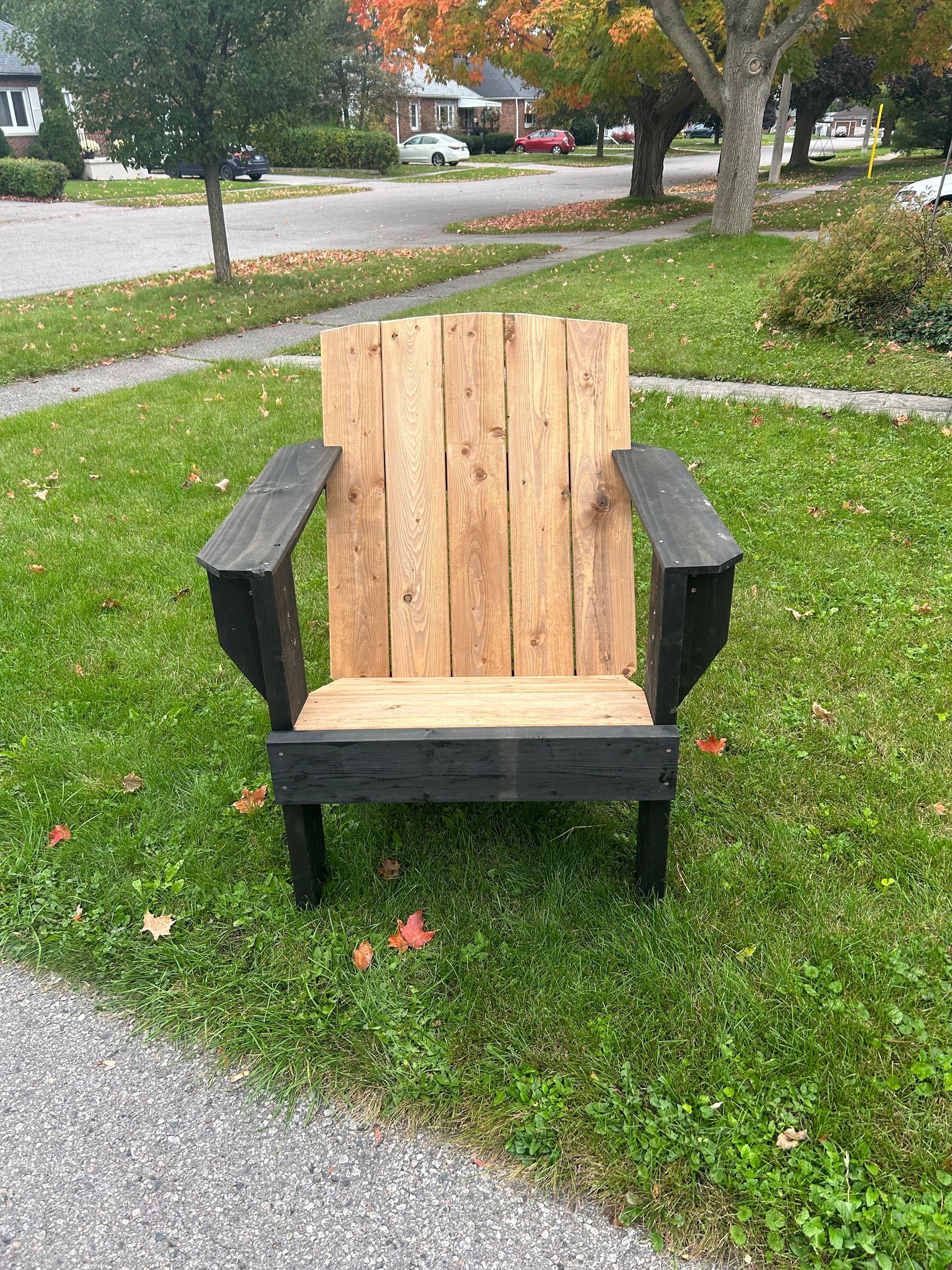 A wooden chair is sitting in the grass next to a sidewalk.