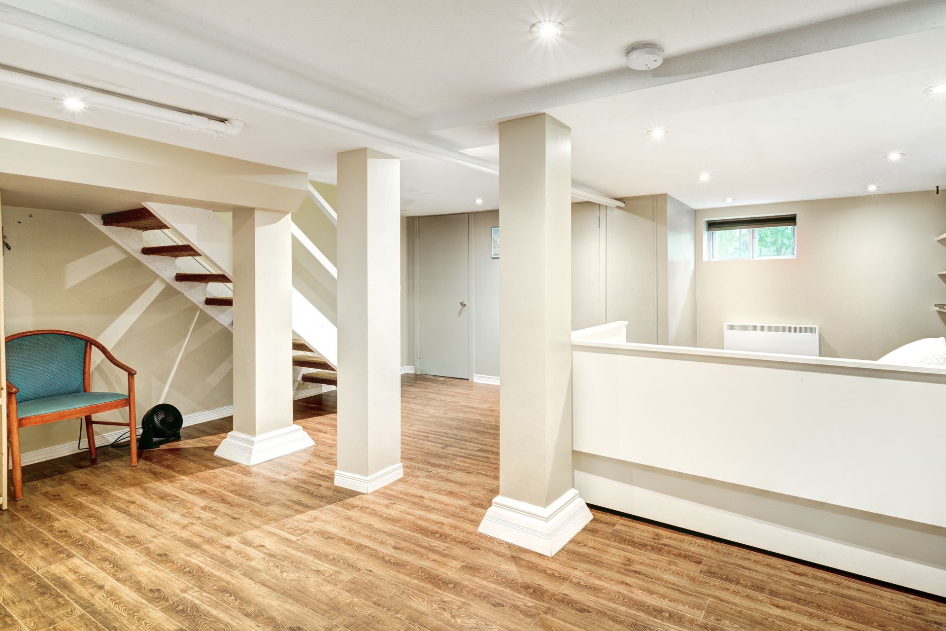 A basement with hardwood floors , stairs , a chair and a white counter.