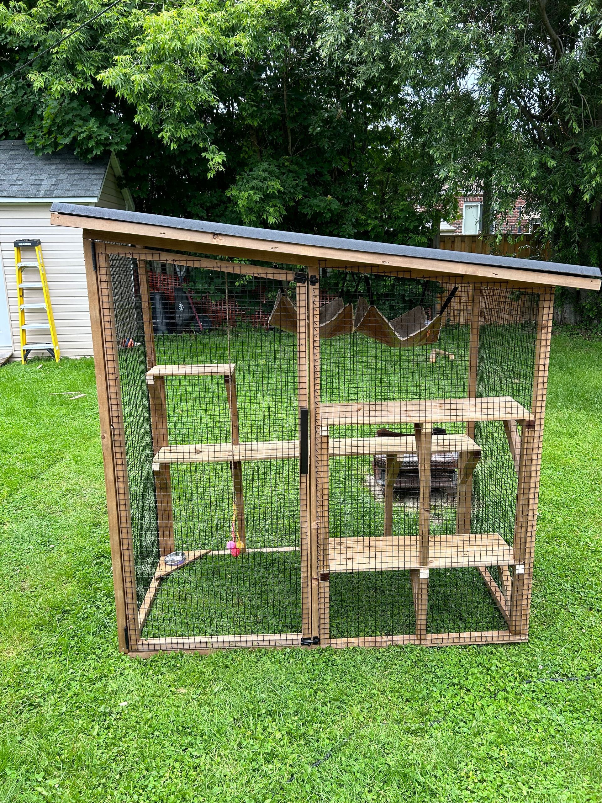 A wooden cat cage is sitting on top of a lush green lawn.