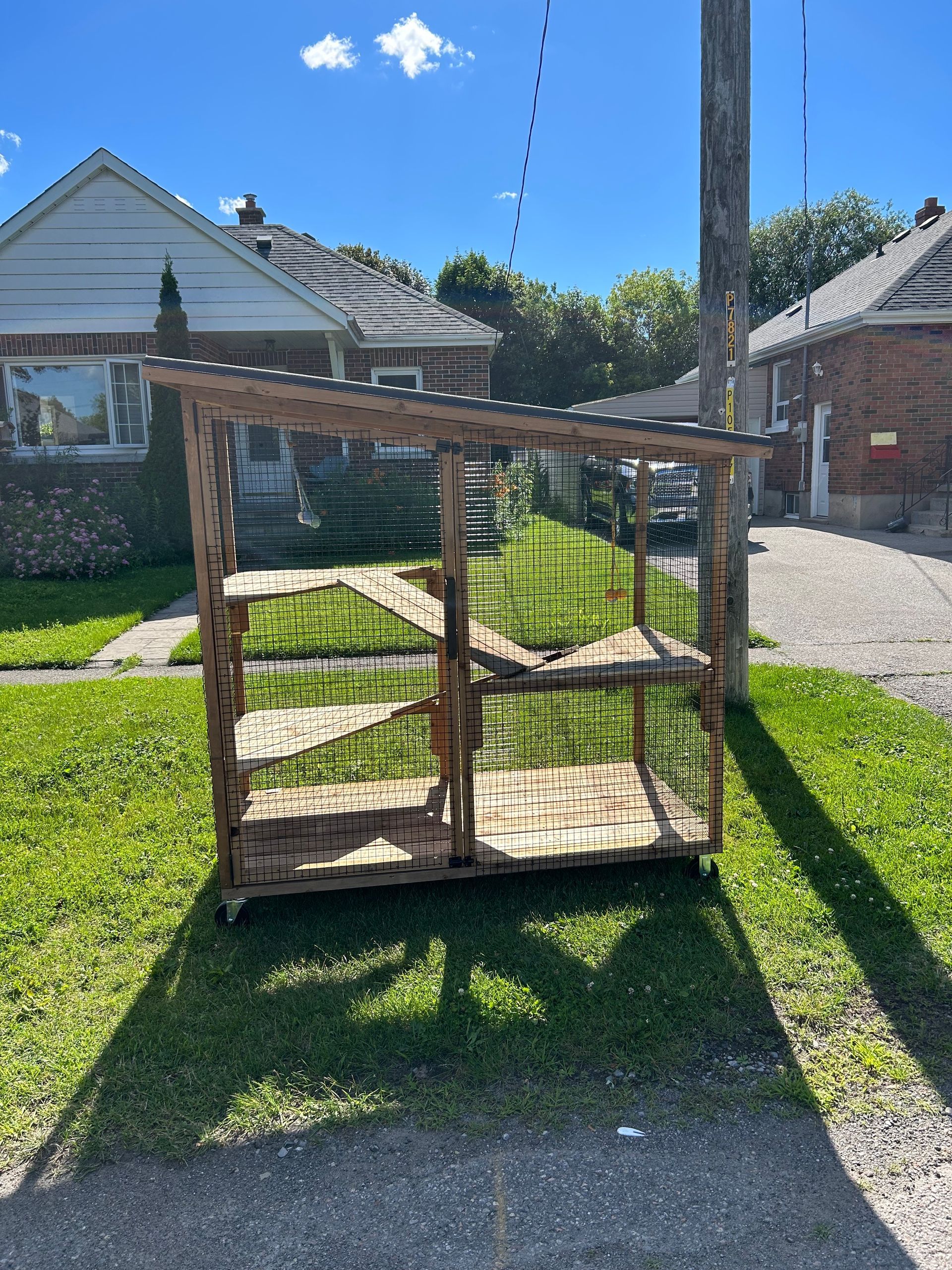 A cage is sitting in the grass in front of a house.