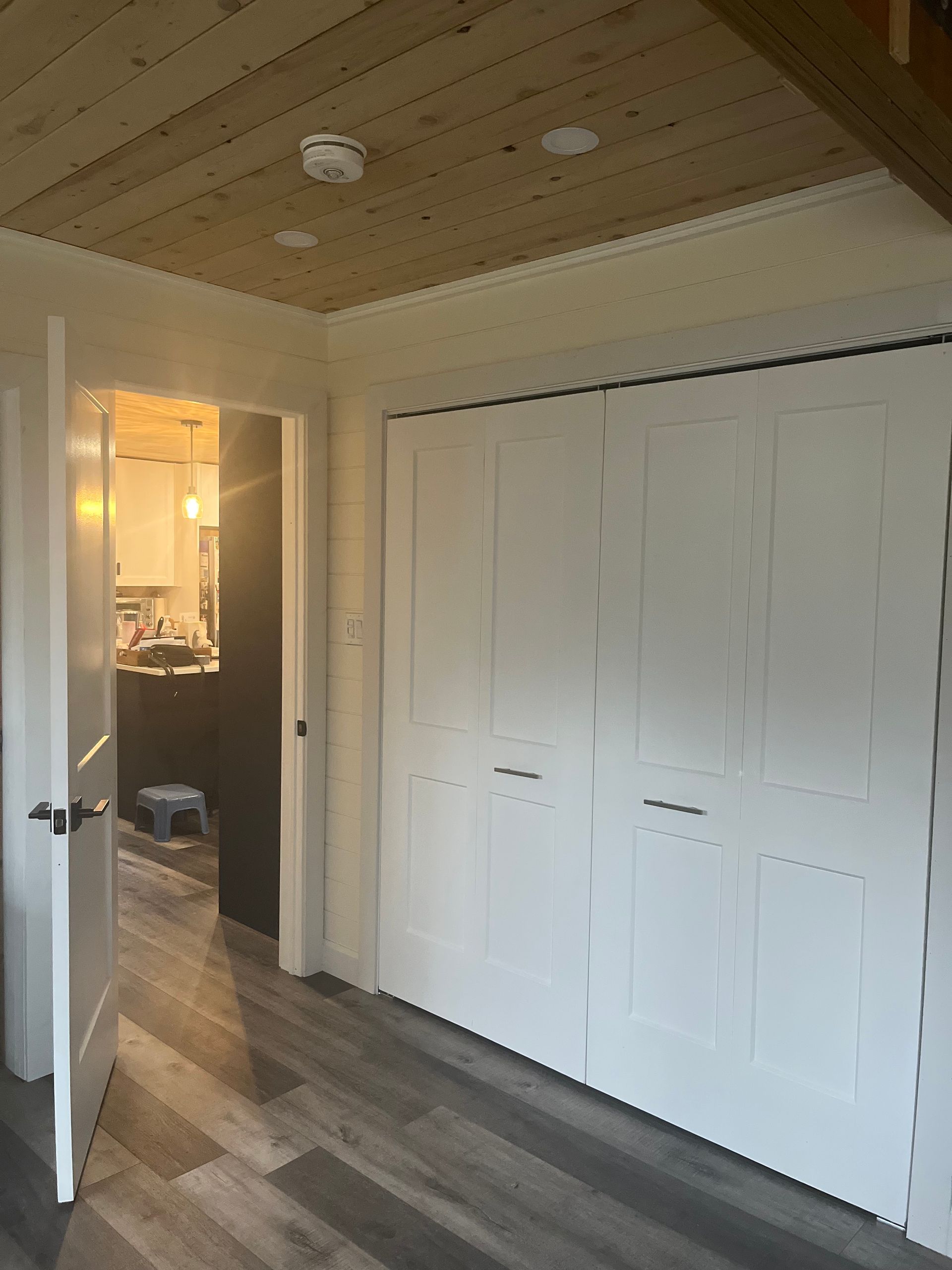 A hallway with white cabinets and a wooden ceiling leading to a kitchen.