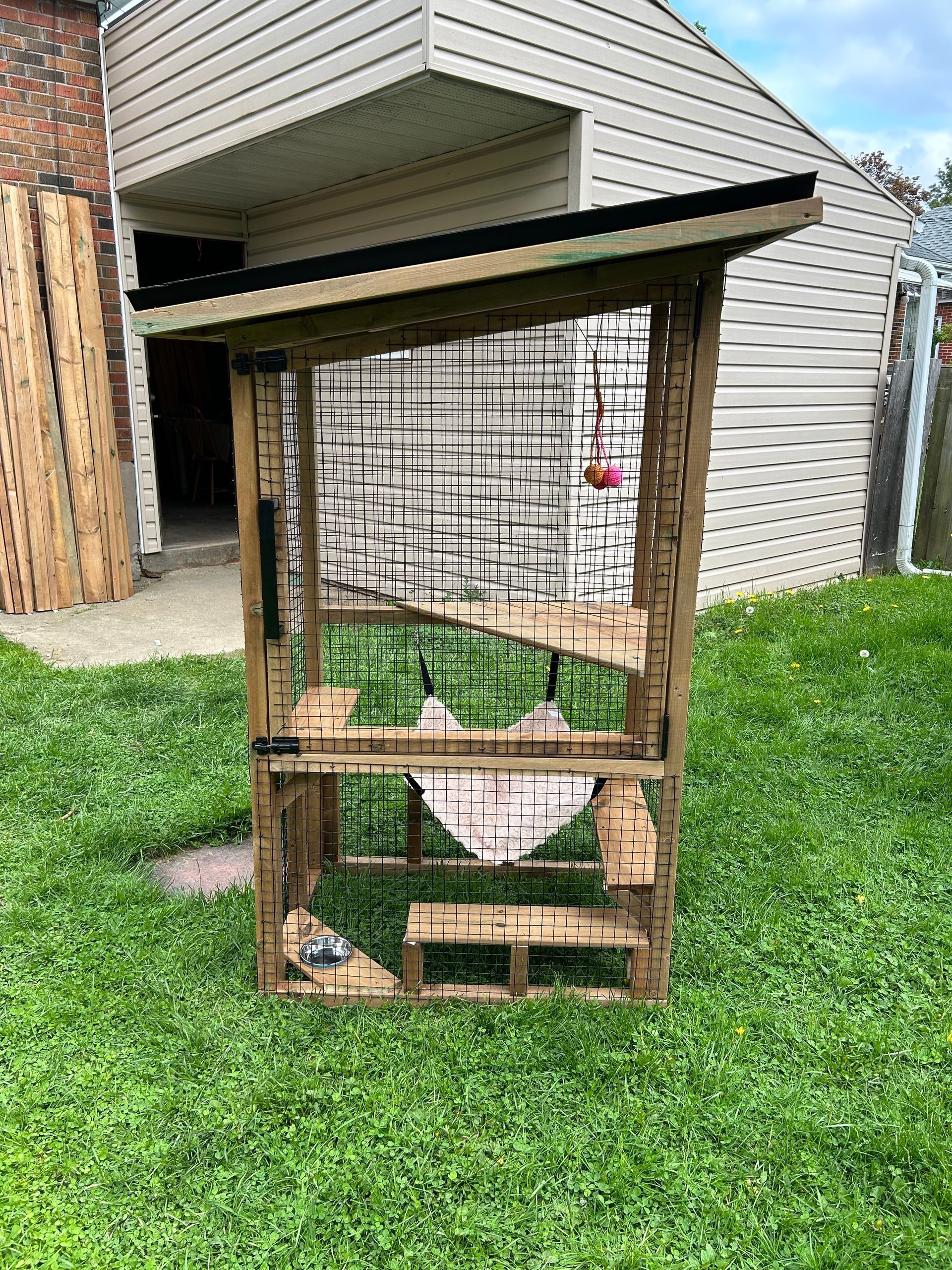 A wooden shelter is sitting in the grass in front of a house.