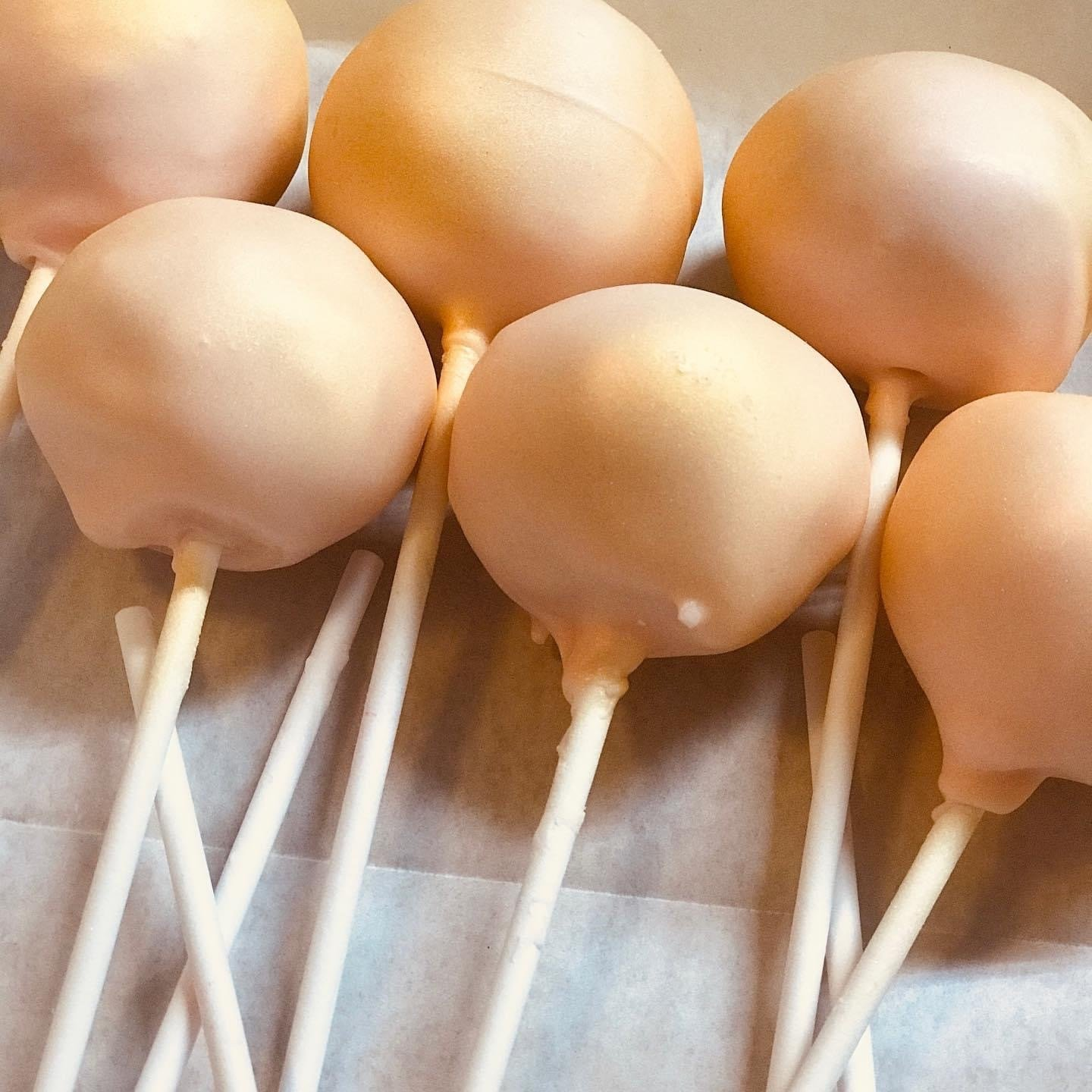 Pink cake pops on white sticks, arranged on parchment paper.