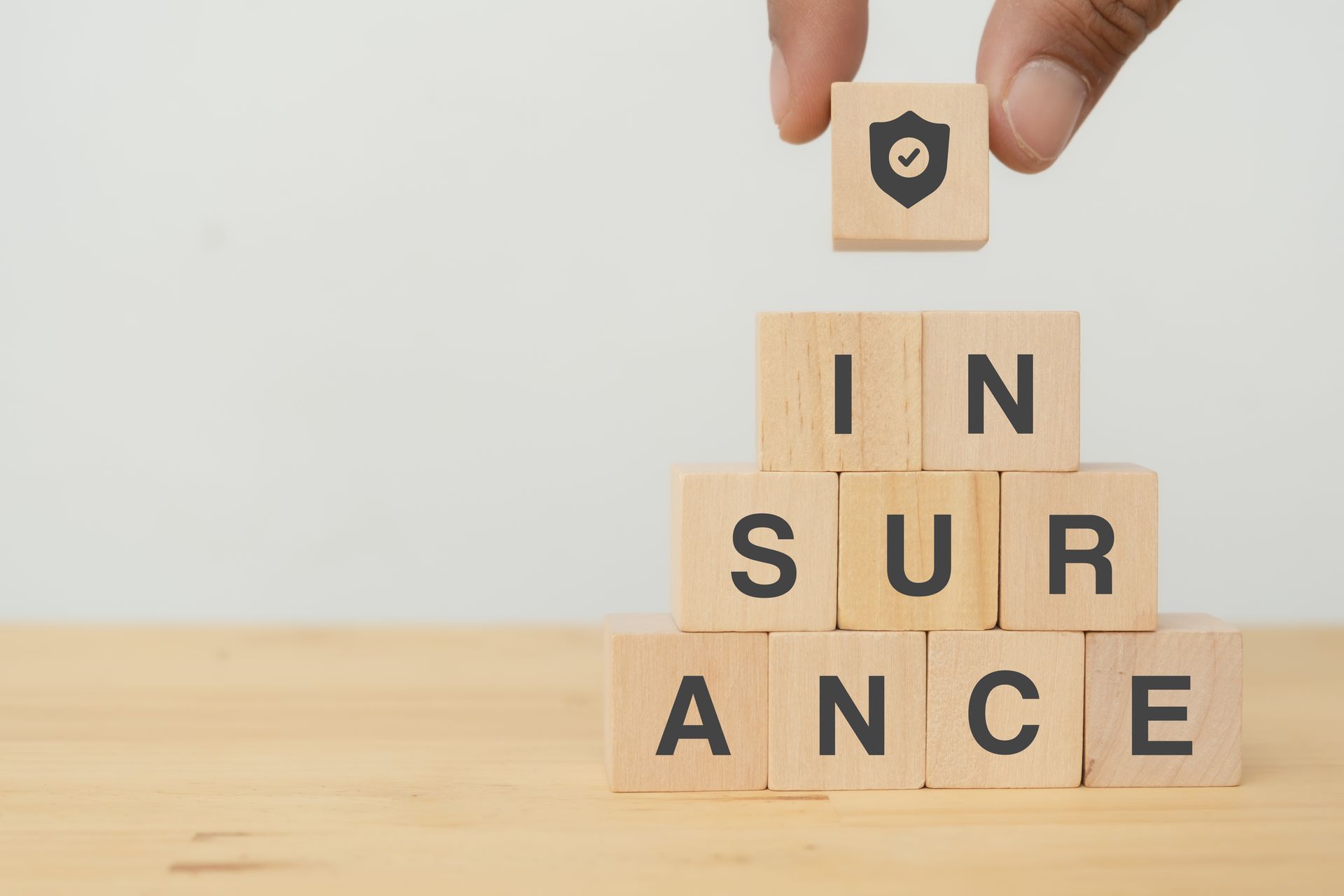 Hand placing a block with a shield icon atop a wooden block pyramid spelling 