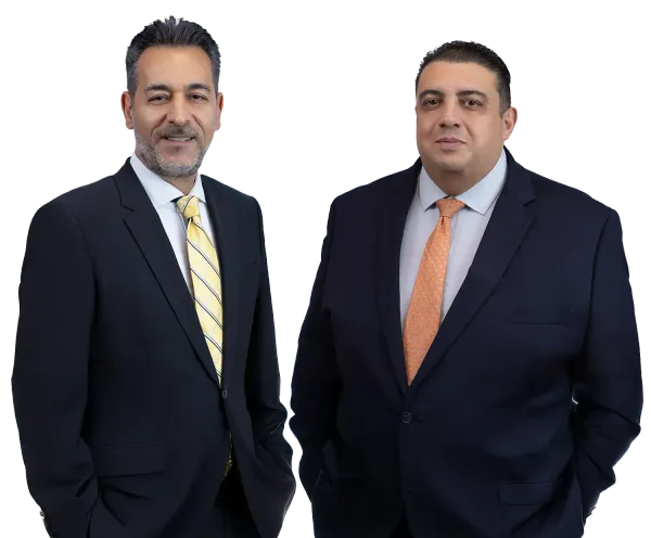 Two men in suits, one with yellow striped tie, other with orange tie, smiling, indoors.