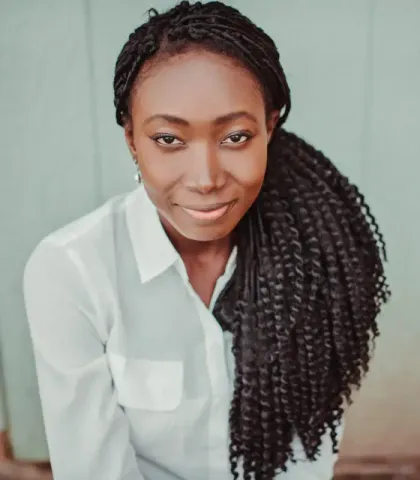 A woman with braids is wearing a white shirt and smiling
