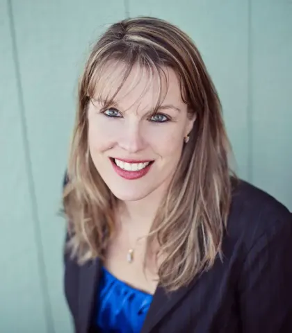 A woman wearing a blue shirt and a black jacket smiles for the camera