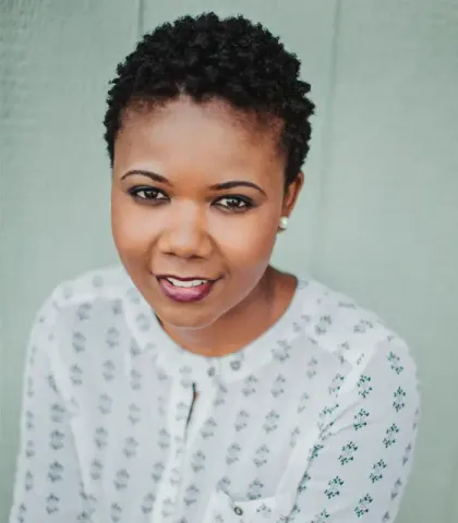 A woman with short hair is wearing a white shirt and smiling for the camera.