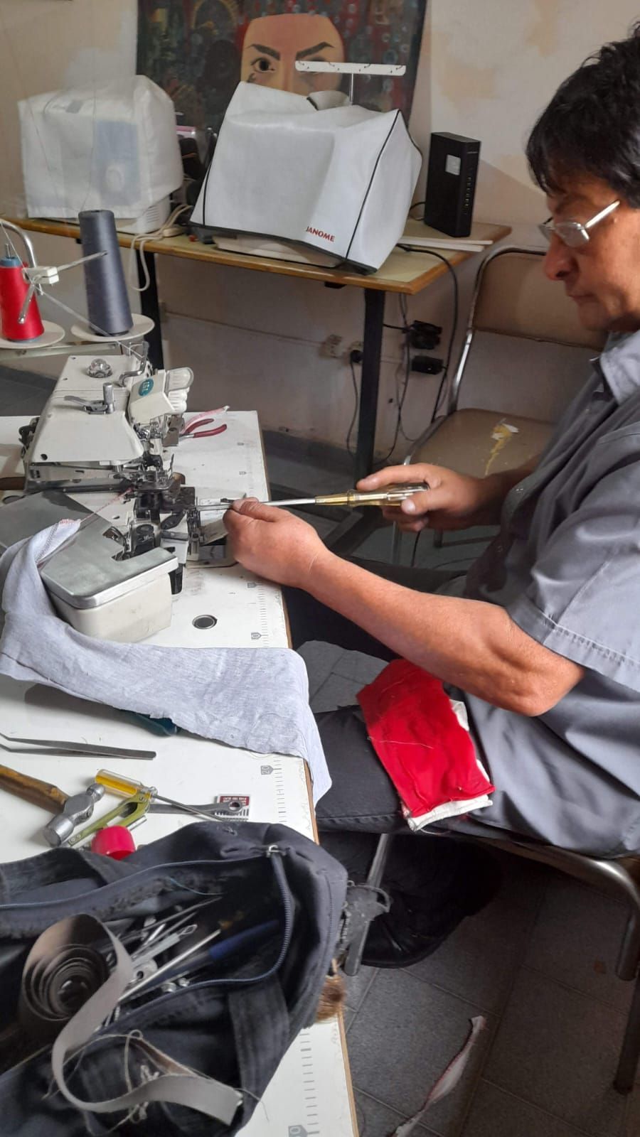 Persona cosiendo en un puesto de trabajo con máquina de coser, tijeras y trozos de tela.