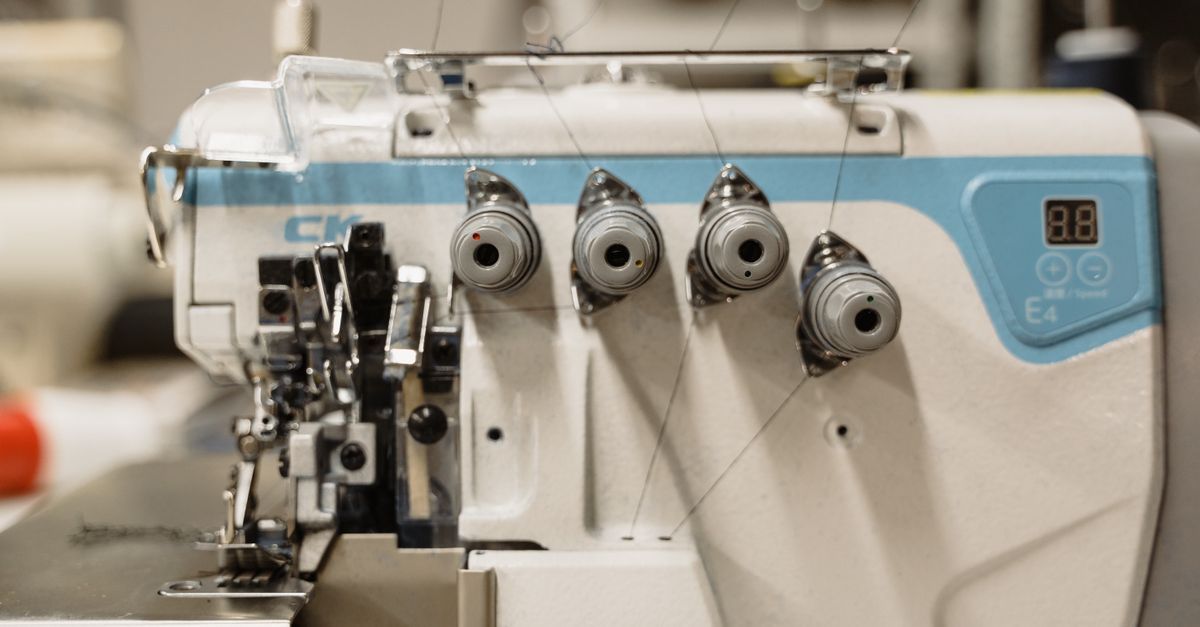 Primer plano de una máquina de coser blanca con detalles azules y múltiples guías de hilo.